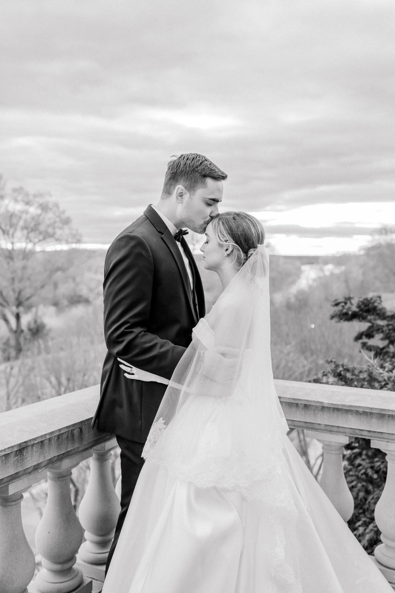 Estate at River Run Wedding in Maidens, VA | Richmond Wedding Photographer | black and white image of a groom kissing his bride on the forehead on the balcony of the Estate at River Run wedding venue