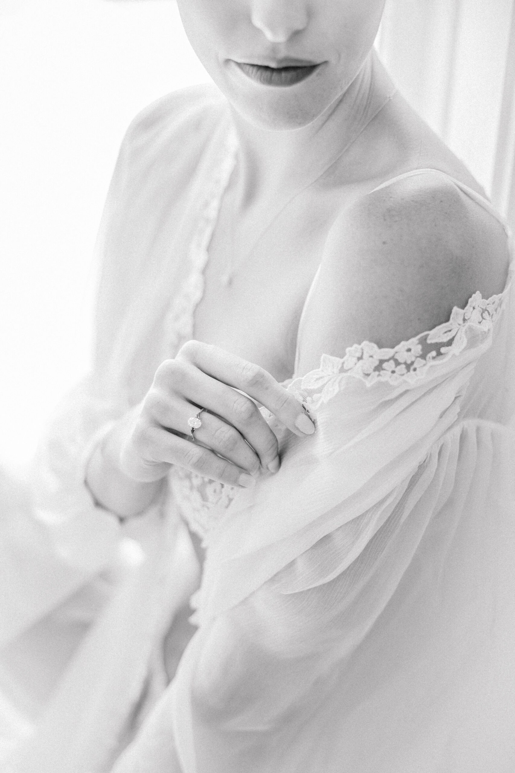 Richmond Boudoir Photographer | romantic floral-filled boudoir session at the Ivy Rose Barn | closeup black and white image of girl showing off her engagement ring as she gently slides her lace-trimmed sheer robe off her shoulder.