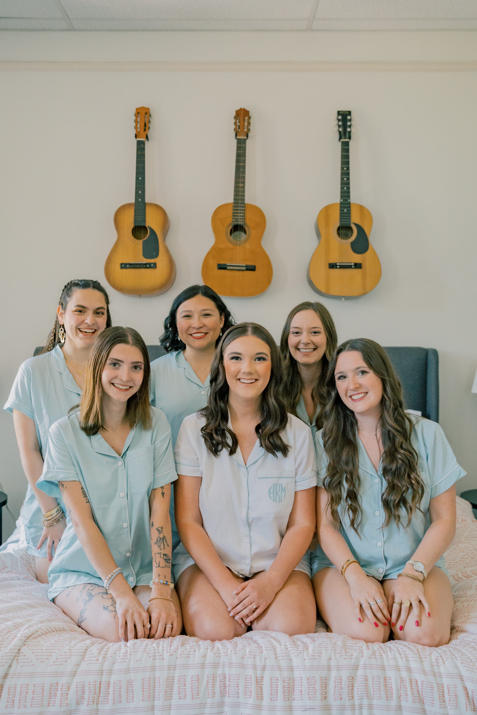 Lynchburg Wedding Photographer | bride in white monogrammed pajamas and bridesmaids in blue pajamas sitting on a bed.