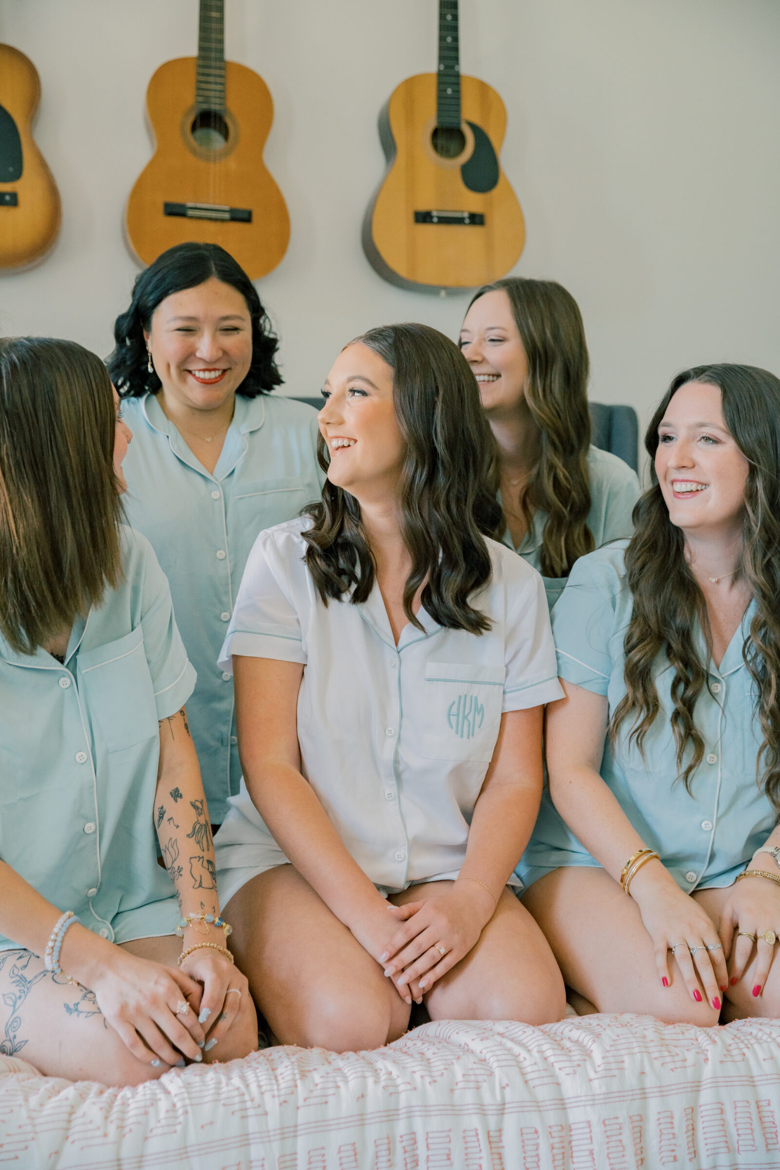 Lynchburg Wedding Photographer | bride in white monogrammed pajamas and bridesmaids in blue pajamas sitting on a bed laughing with each other