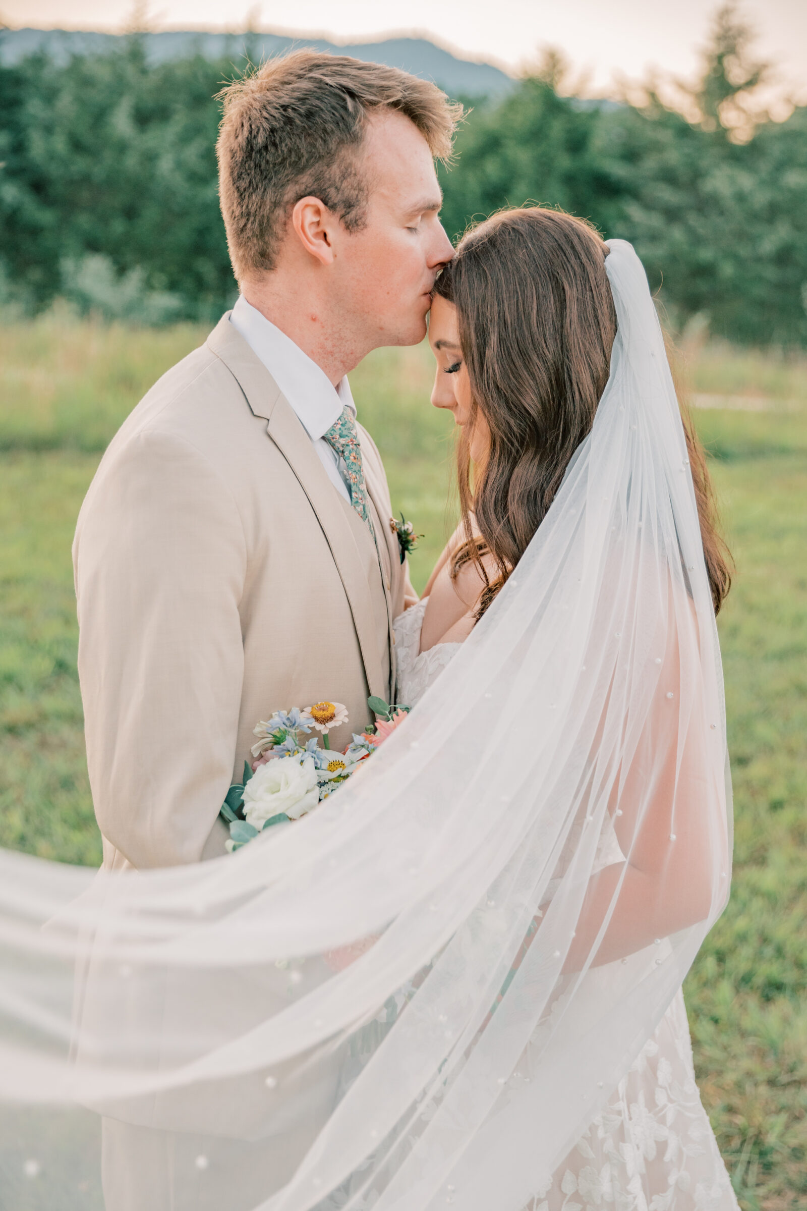 Three Oaks Manor Wedding in Madison Heights, VA | Virginia Wedding Photographer | groom tenderly kisses his bride's forehead while her white pearl veil blows softly in the wind