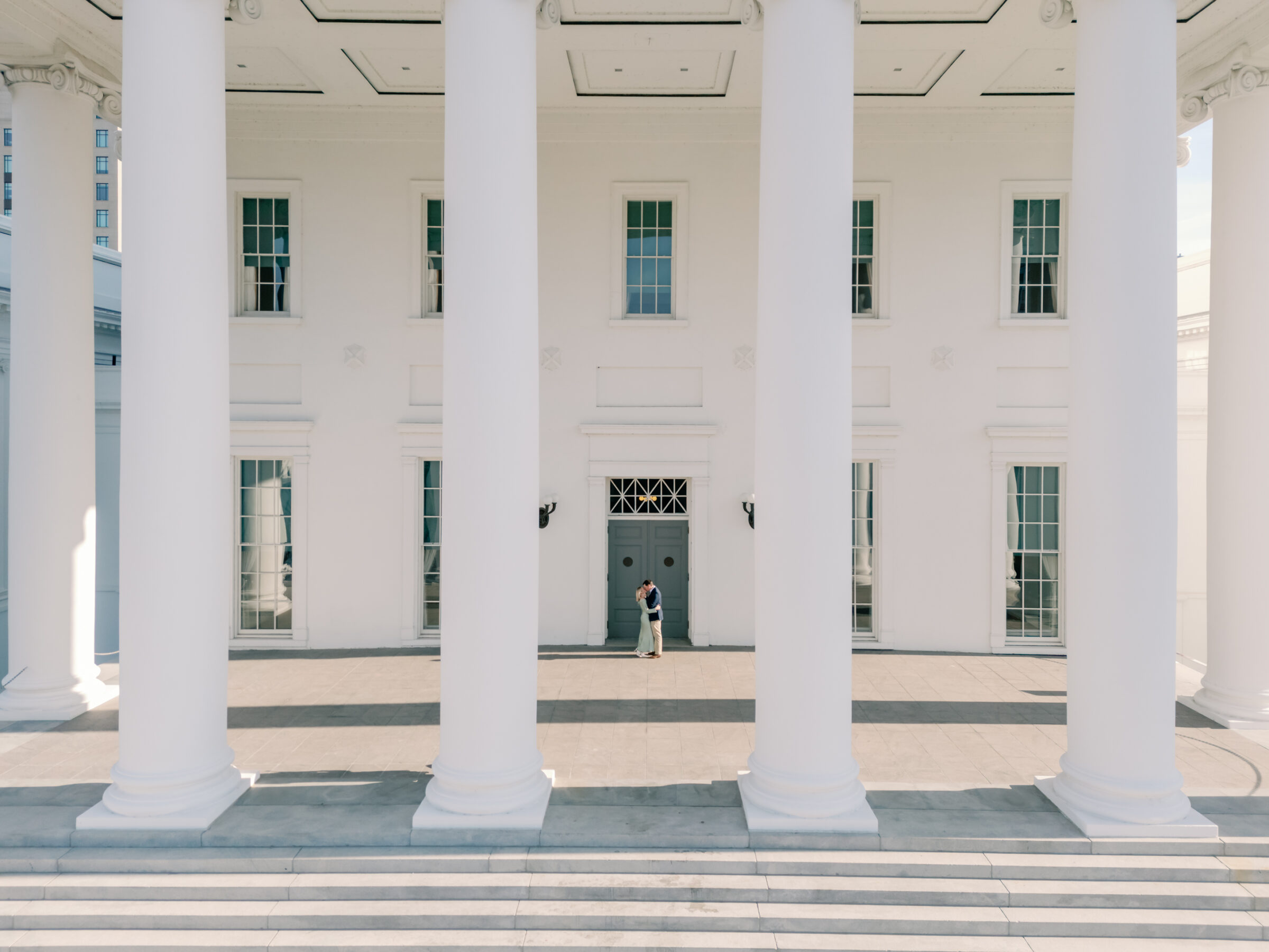 A newly engaged couple shares a romantic moment beneath the grand white columns of the Virginia State Capitol in Richmond, Virginia. The neoclassical architecture provides an elegant and timeless backdrop, perfect for engagement photos. Captured by a Richmond engagement photographer, this image beautifully highlights one of the most historic wedding and portrait locations in Virginia.