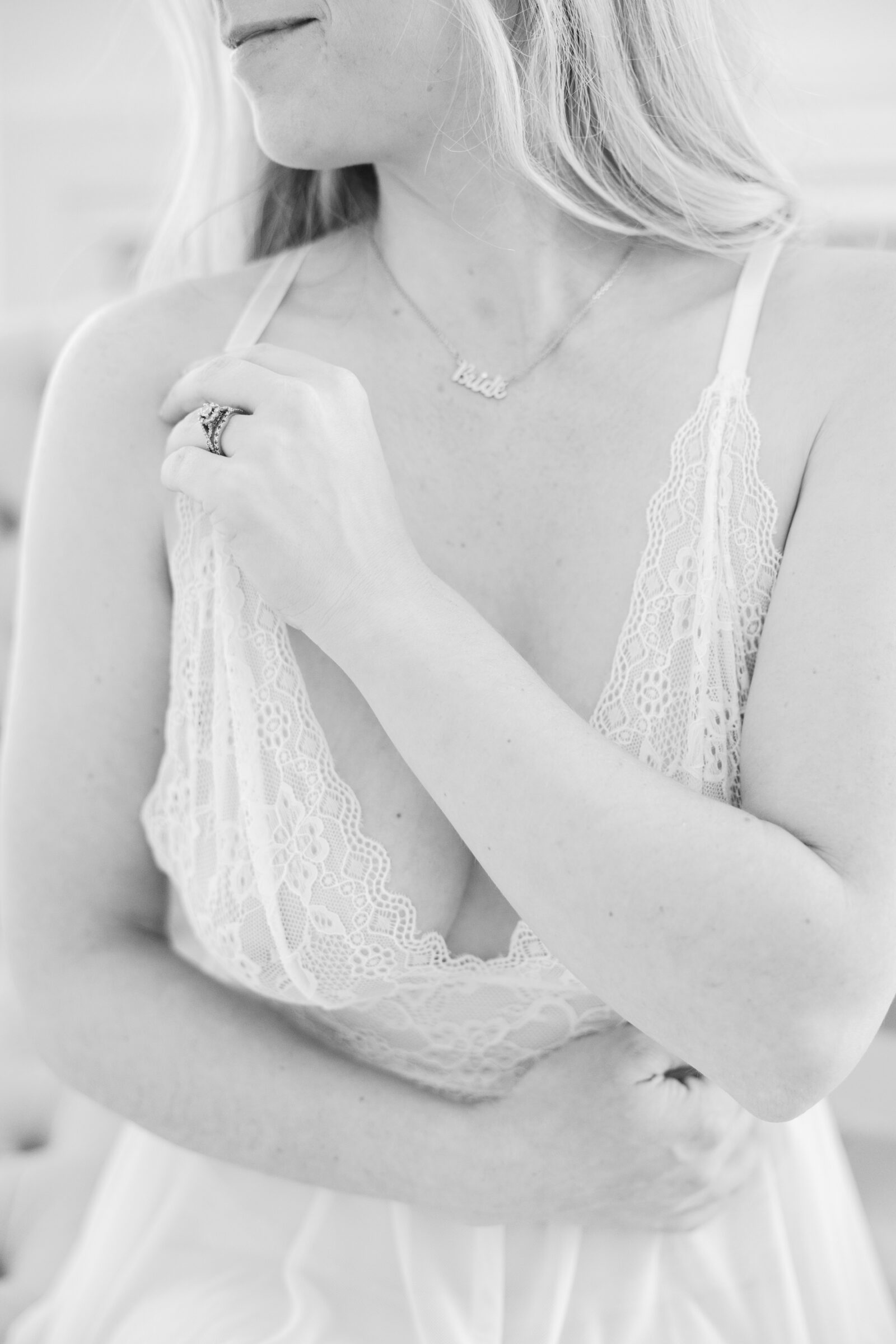 Romantic Bridal Boudoir Session in Richmond VA | closeup black and white image of a girl in white lace lingerie touching her bra strap while wearing an engagement ring