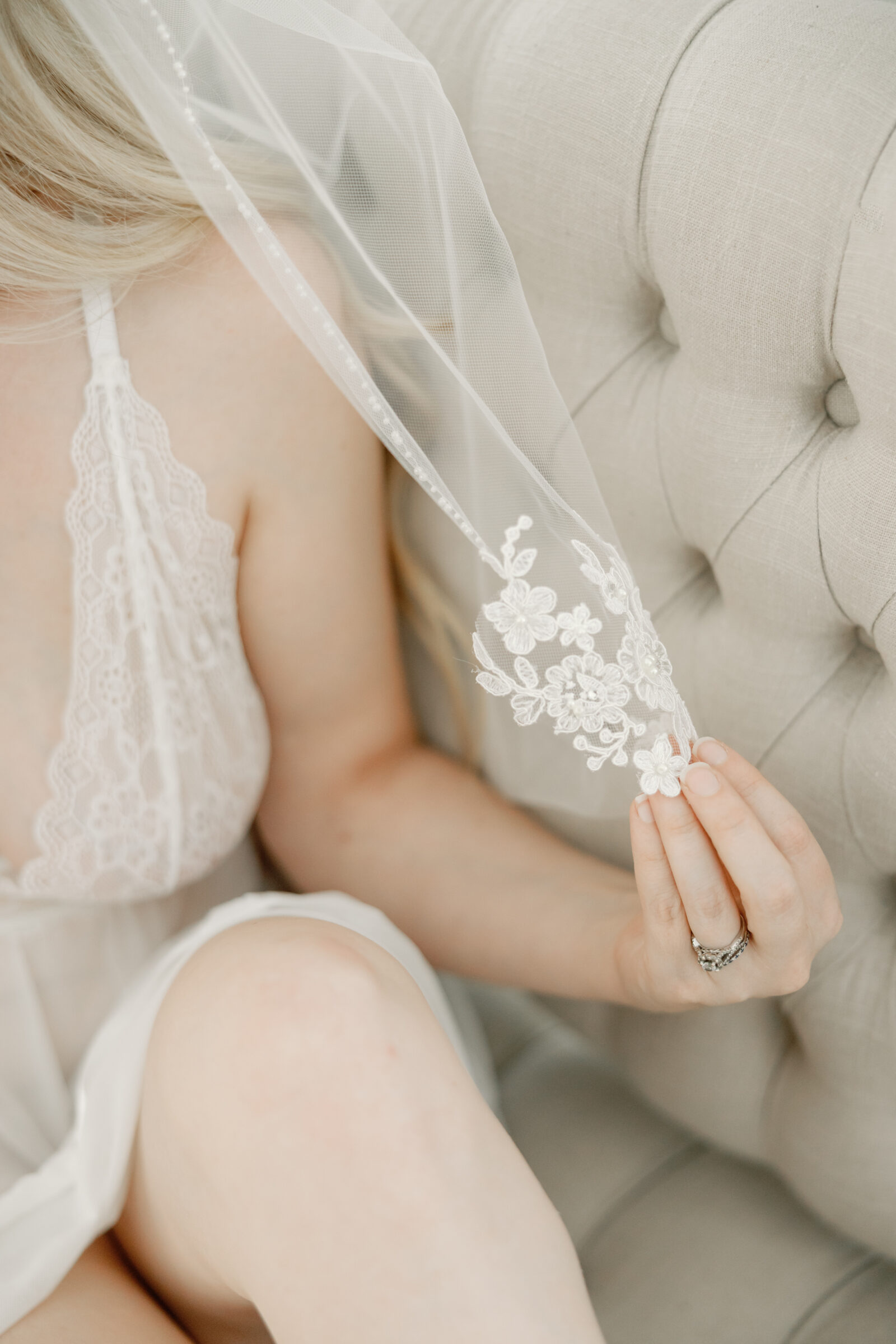 Romantic Bridal Boudoir Session in Richmond VA | detail photo of a girl in white lace lingerie holding a lace bridal veil with her fingers. She has an engagement ring on.