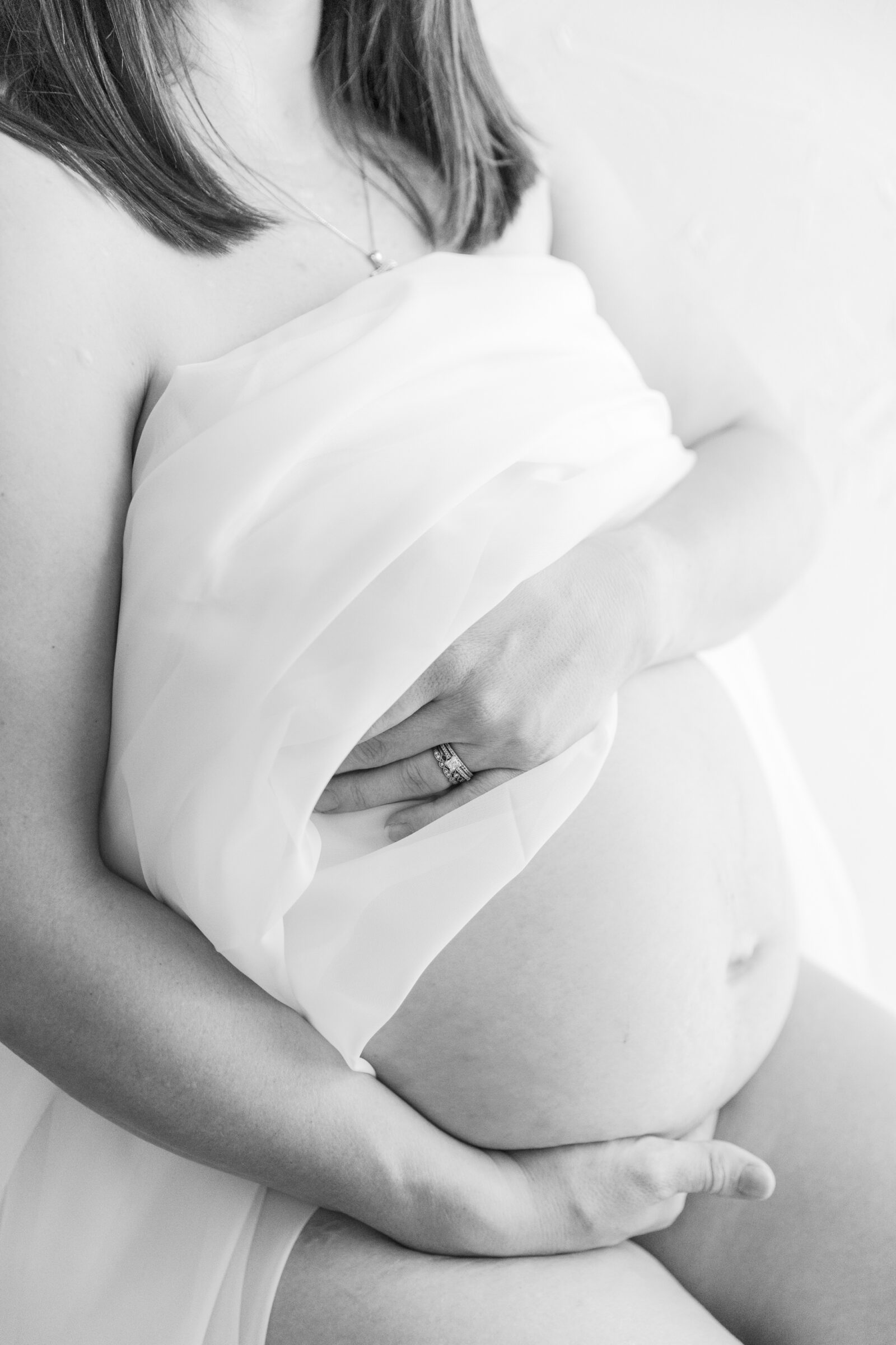Richmond Maternity Boudoir Session | black and white image of pregnant woman with a white cloth over her breasts, cradling her baby bump