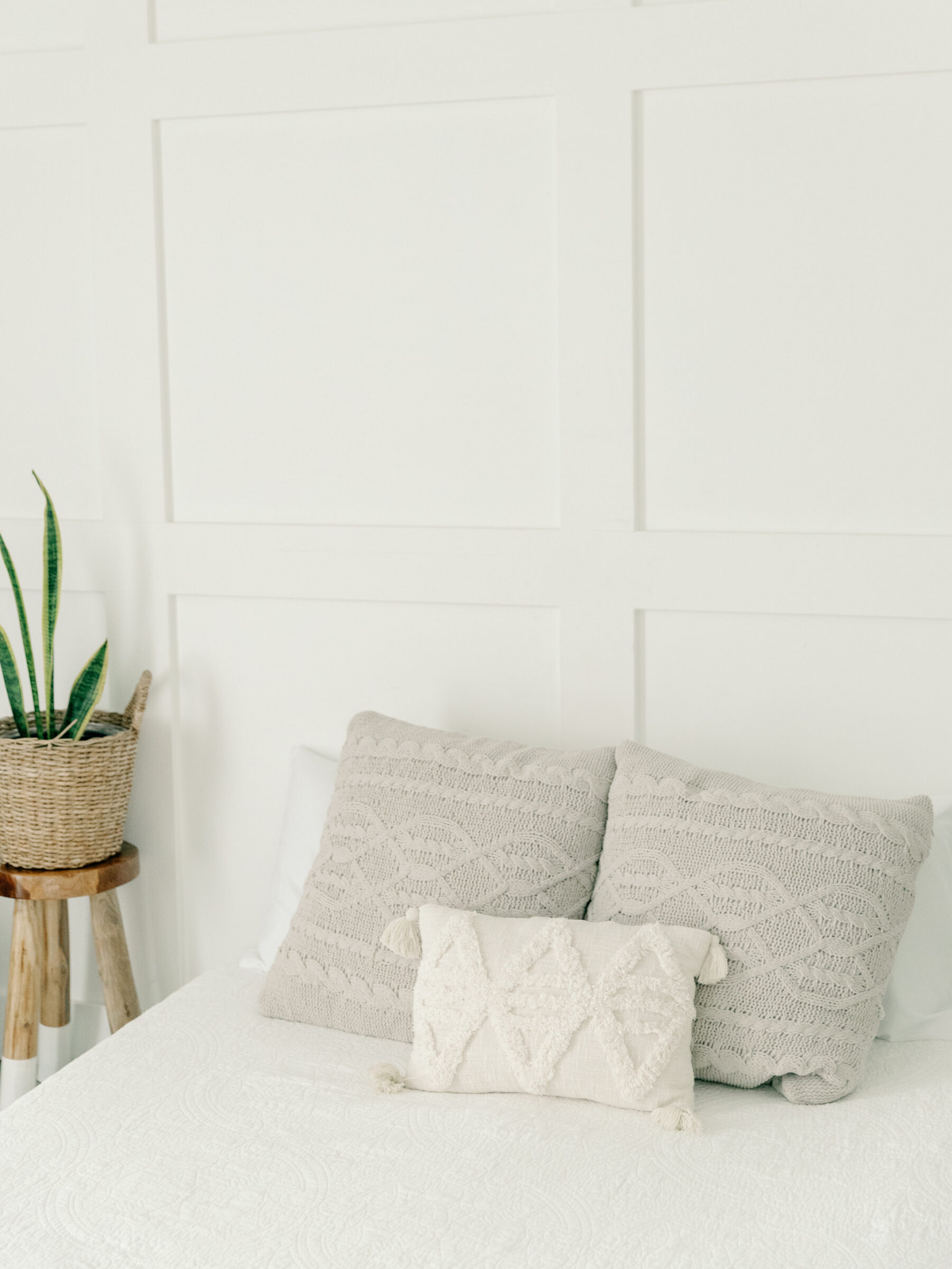 A cozy corner of Carbone Studios in Richmond, VA, showcasing a bed with white linens and textured pillows. A potted plant sits on a small wooden stool beside the bed, adding a natural touch to the minimalist studio design.