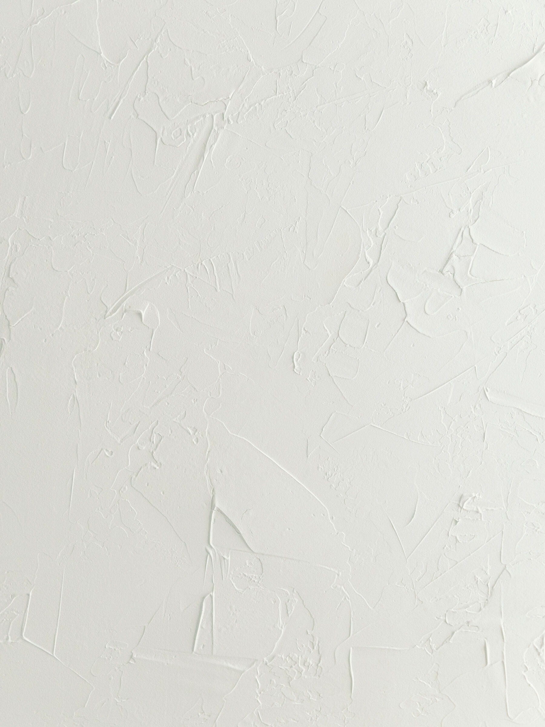 A close-up of a textured white wall at Carbone Studios, a boudoir photography studio in Richmond, VA. The wall features a subtle plaster design with soft, uneven textures that add depth and visual interest to the minimalist space.