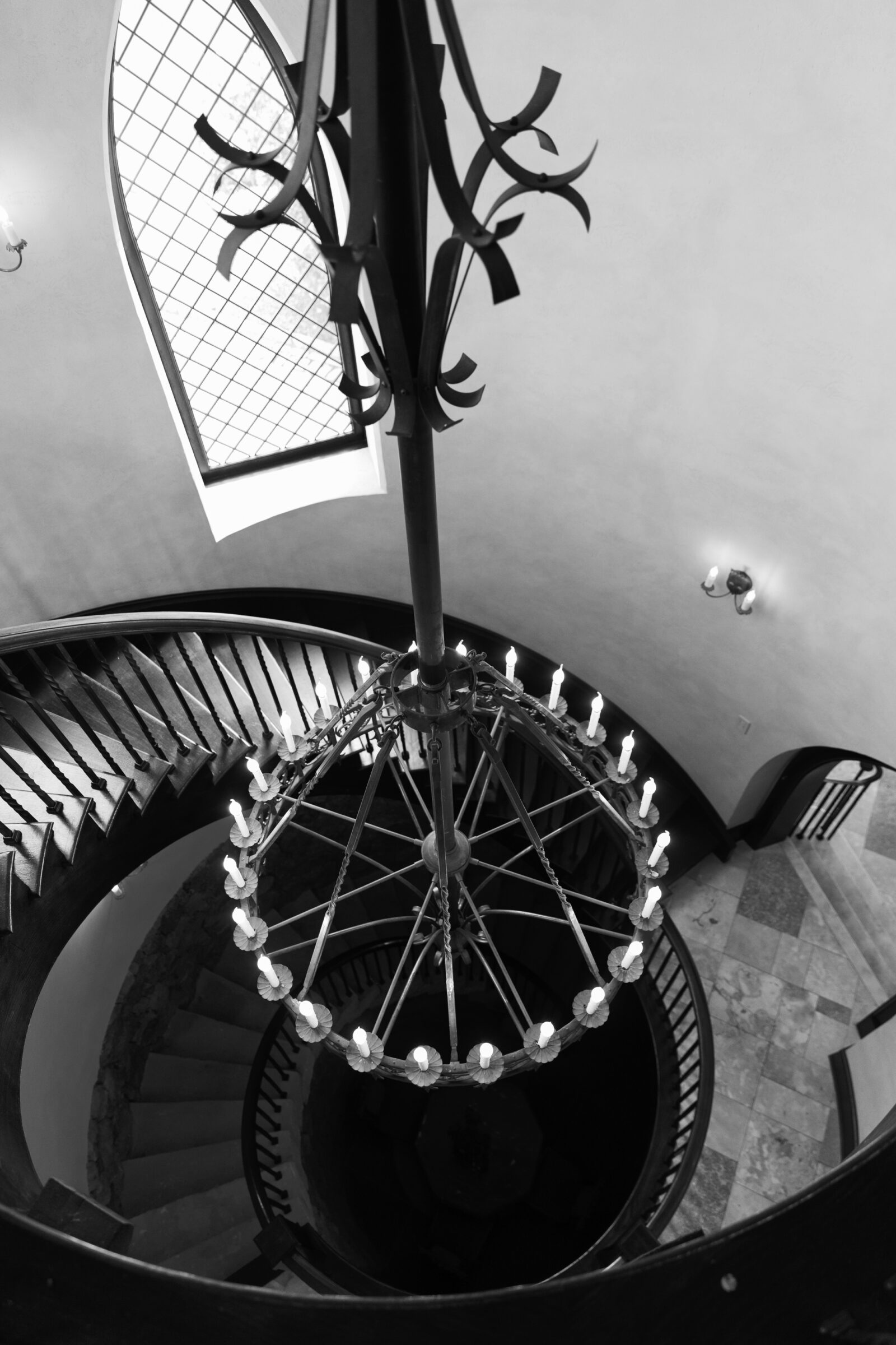 A breathtaking view of the grand spiral staircase inside Dover Hall in Richmond, VA, showcasing its elegant wrought-iron chandelier and intricate stone steps, framed by a stunning arched window.