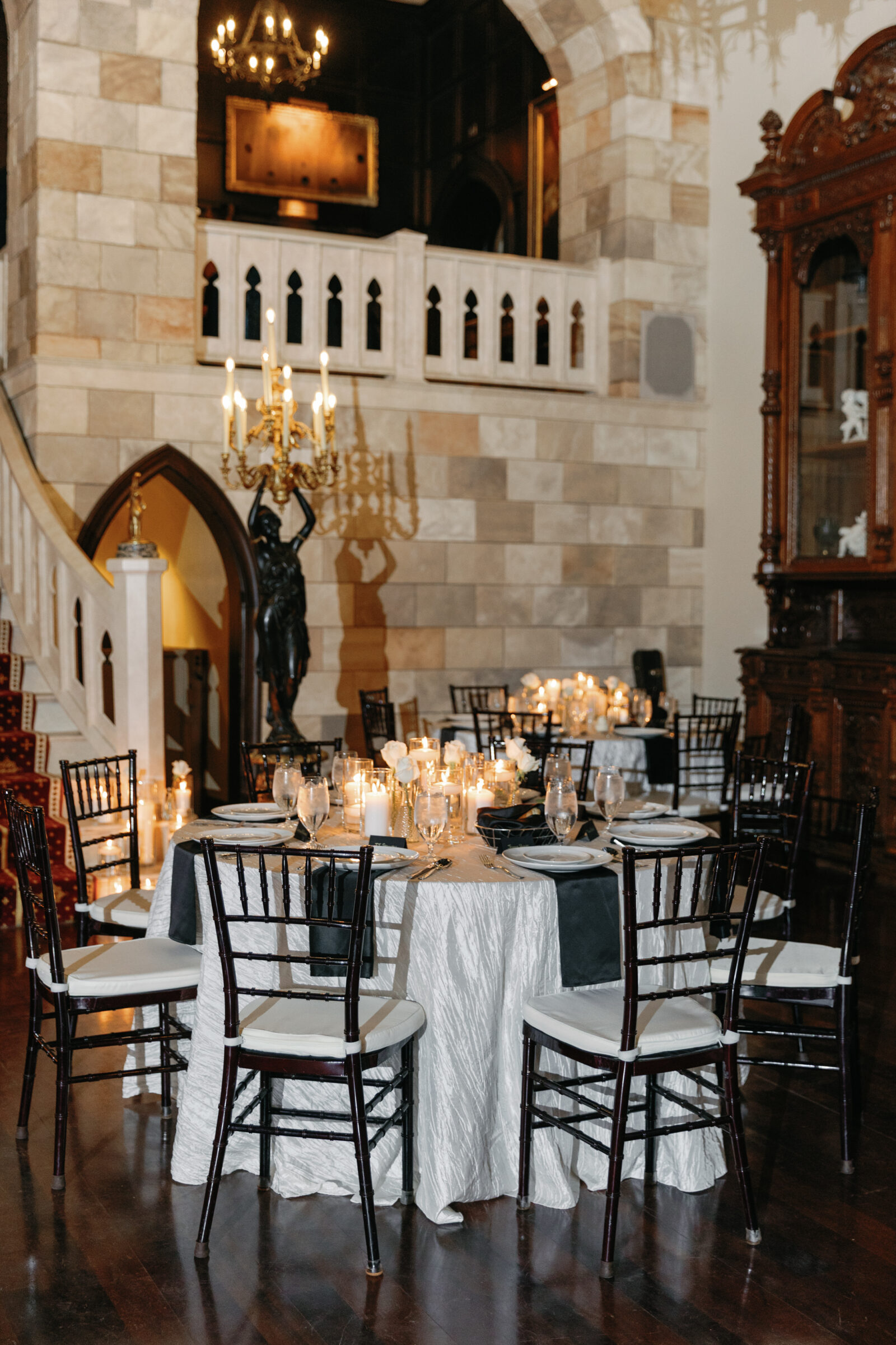 An elegant reception setup at Dover Hall Richmond VA featuring a beautifully decorated table with white linens, black napkins, and flickering candles, creating a romantic atmosphere. The grand staircase in the background adds to the sophisticated charm of the venue.