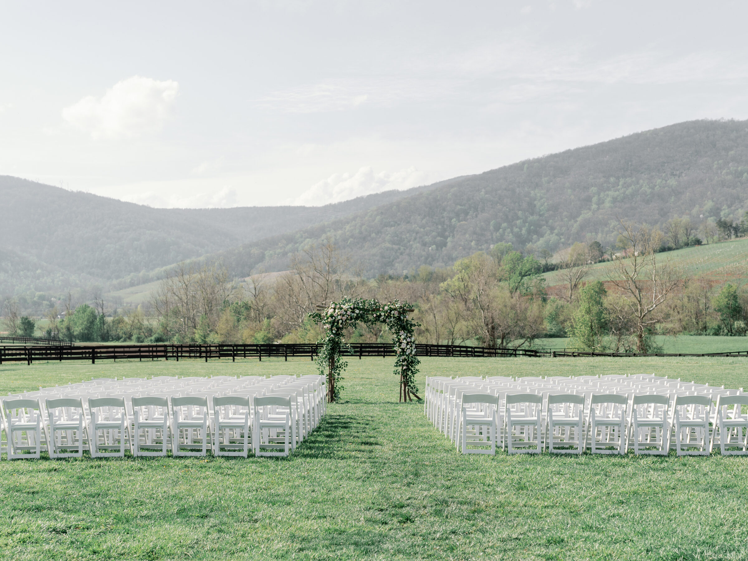 Outdoor wedding ceremony setup at King Family Vineyards, featuring rows of white chairs and a floral-covered arch with the Blue Ridge Mountains in the background.