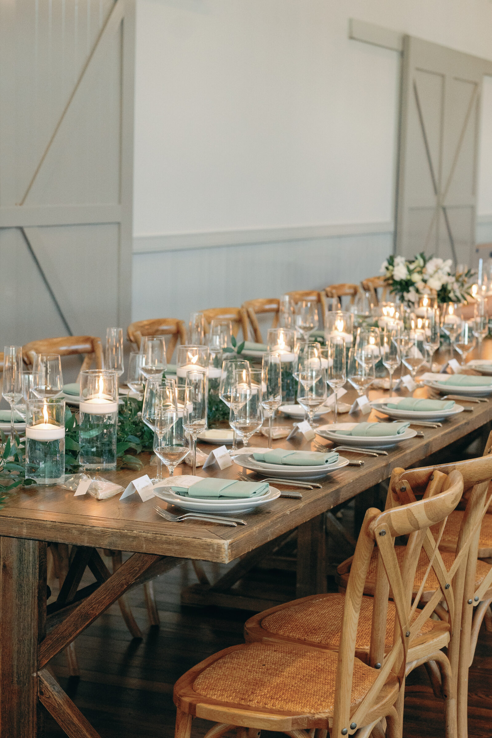 A beautifully set long wooden table with mint green napkins, glass candle holders, and lush greenery for a wedding reception at King Family Vineyards, showcasing an elegant and rustic atmosphere.