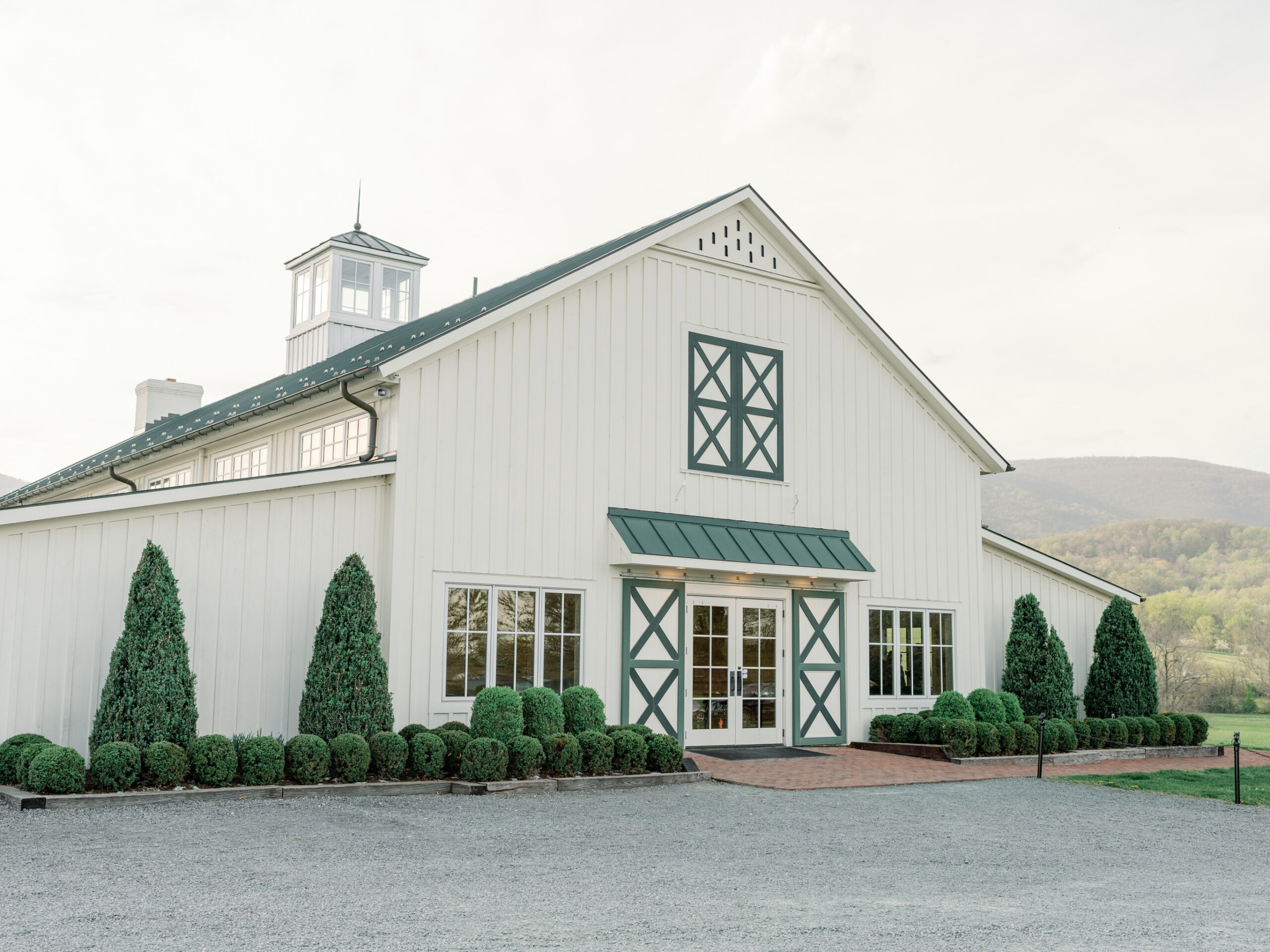 Exterior view of King Family Vineyards wedding venue in Charlottesville, VA, featuring the elegant white barn with green trim, neatly manicured hedges, and the backdrop of rolling hills.
