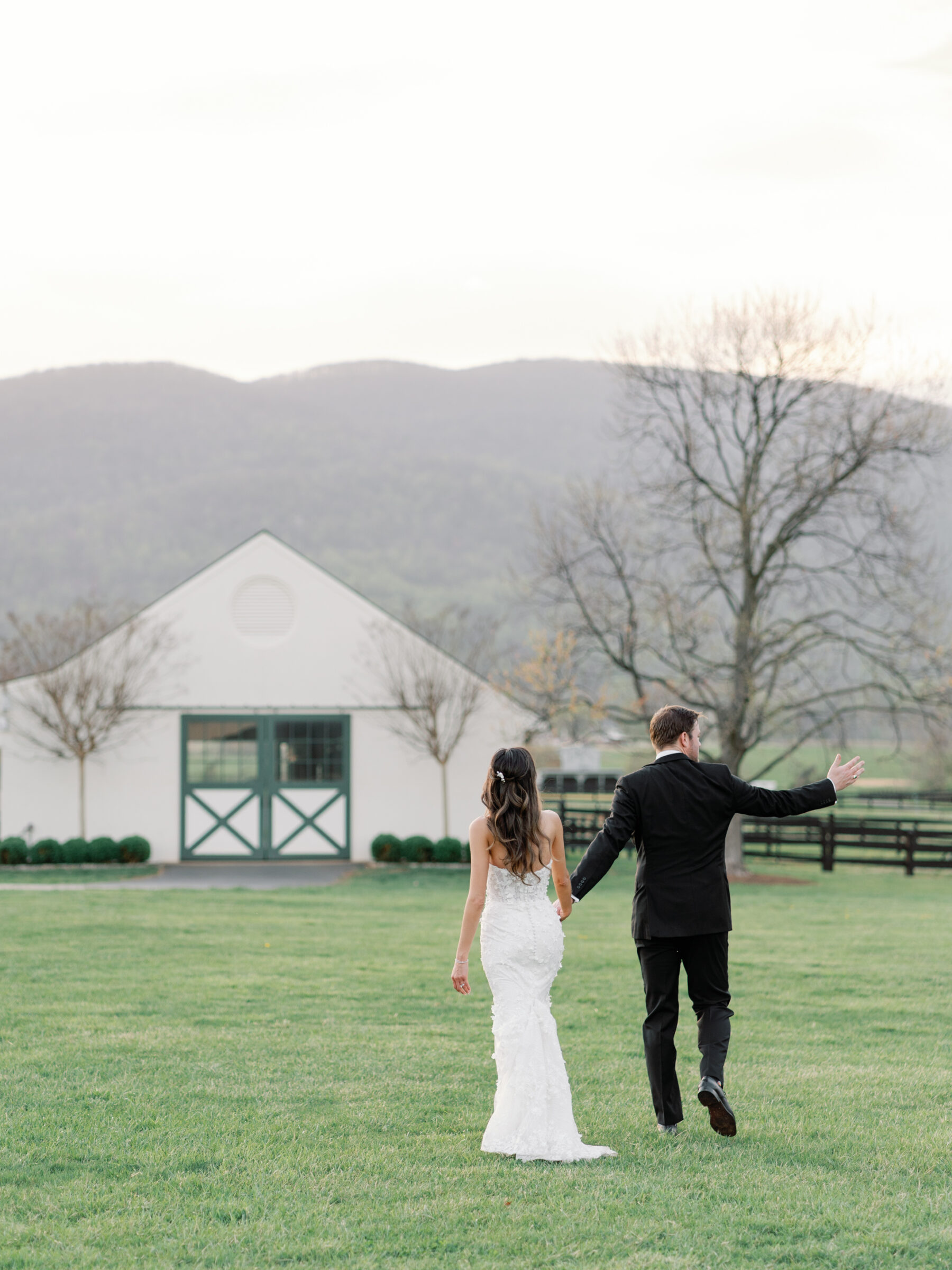 Bride and groom walking hand-in-hand across the vineyard grounds at King Family Vineyards, with the picturesque white barn and rolling hills in the background.
