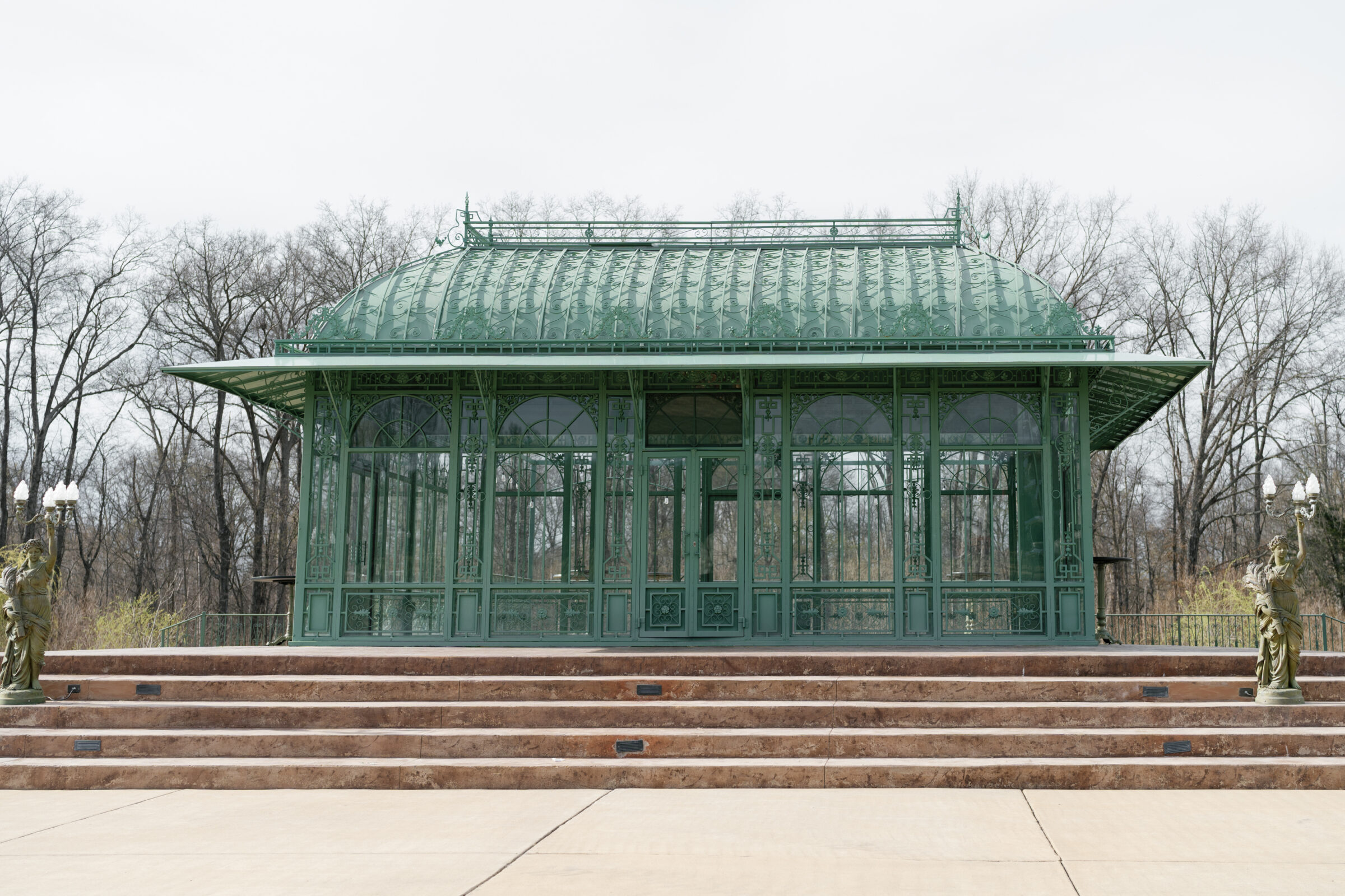 The wrought-iron gazebo at Morais Vineyards is framed by stone steps, with statues holding candelabras on either side, set against a backdrop of bare trees in early spring.