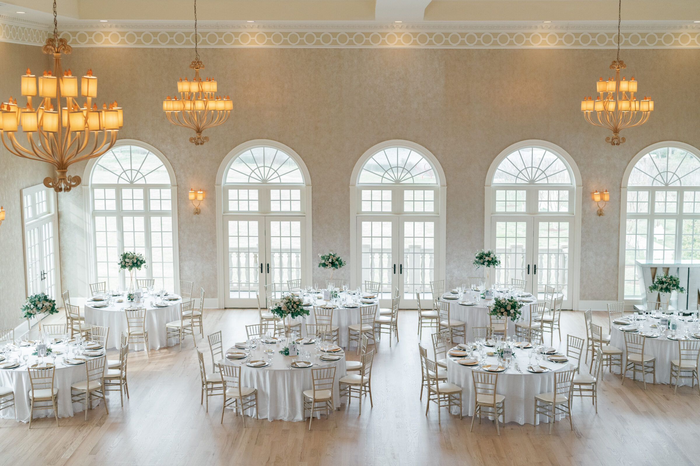 An elegant wedding reception at Morais Vineyards, featuring circular tables with white linens and floral centerpieces, bathed in soft natural light from large windows overlooking the venue’s grounds.