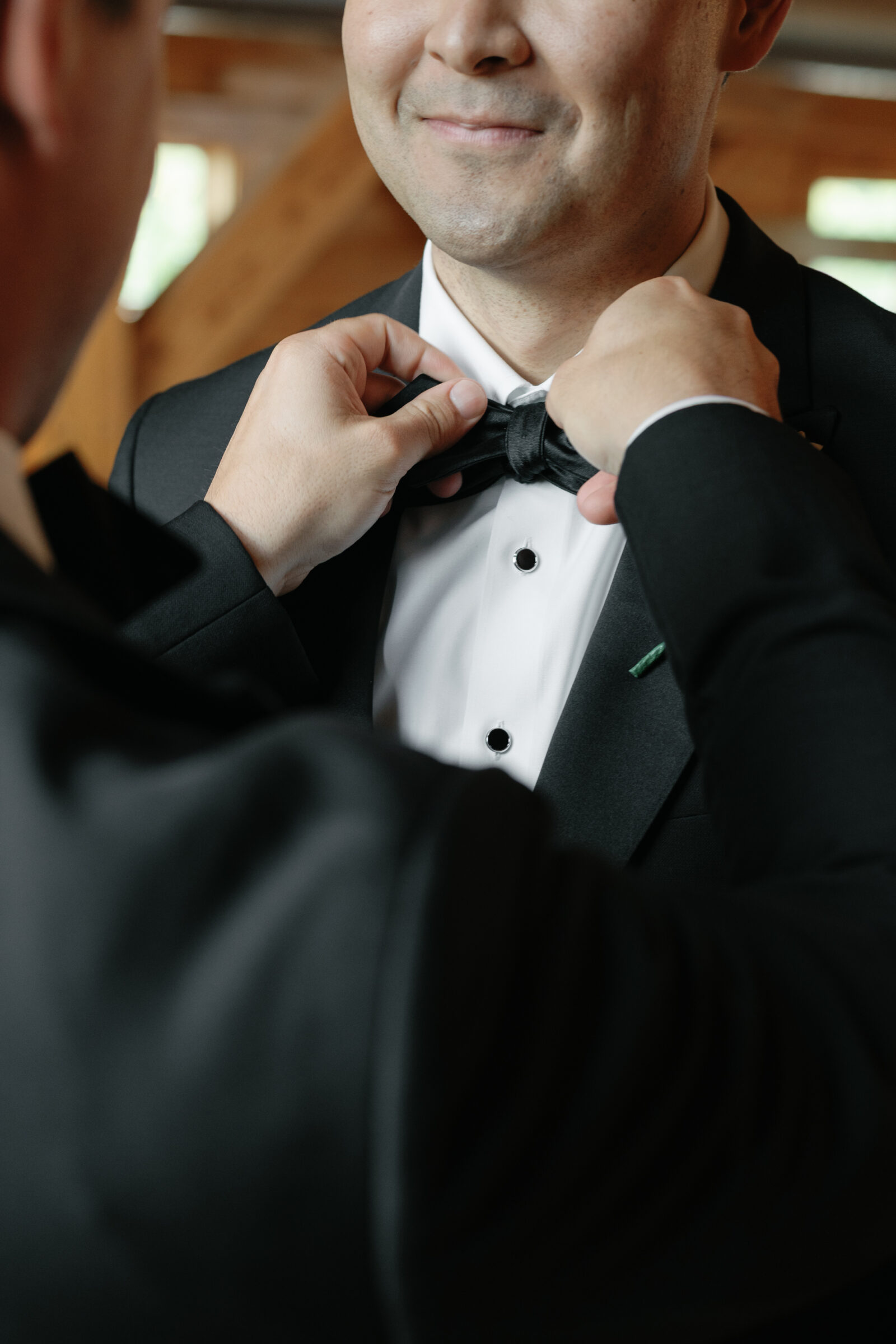 A groom’s best man adjusts his bow tie, helping him prepare for the day. The groom smiles warmly as the final touches are made, capturing a moment of support and camaraderie before the ceremony at the Middleburg Barn Wedding.