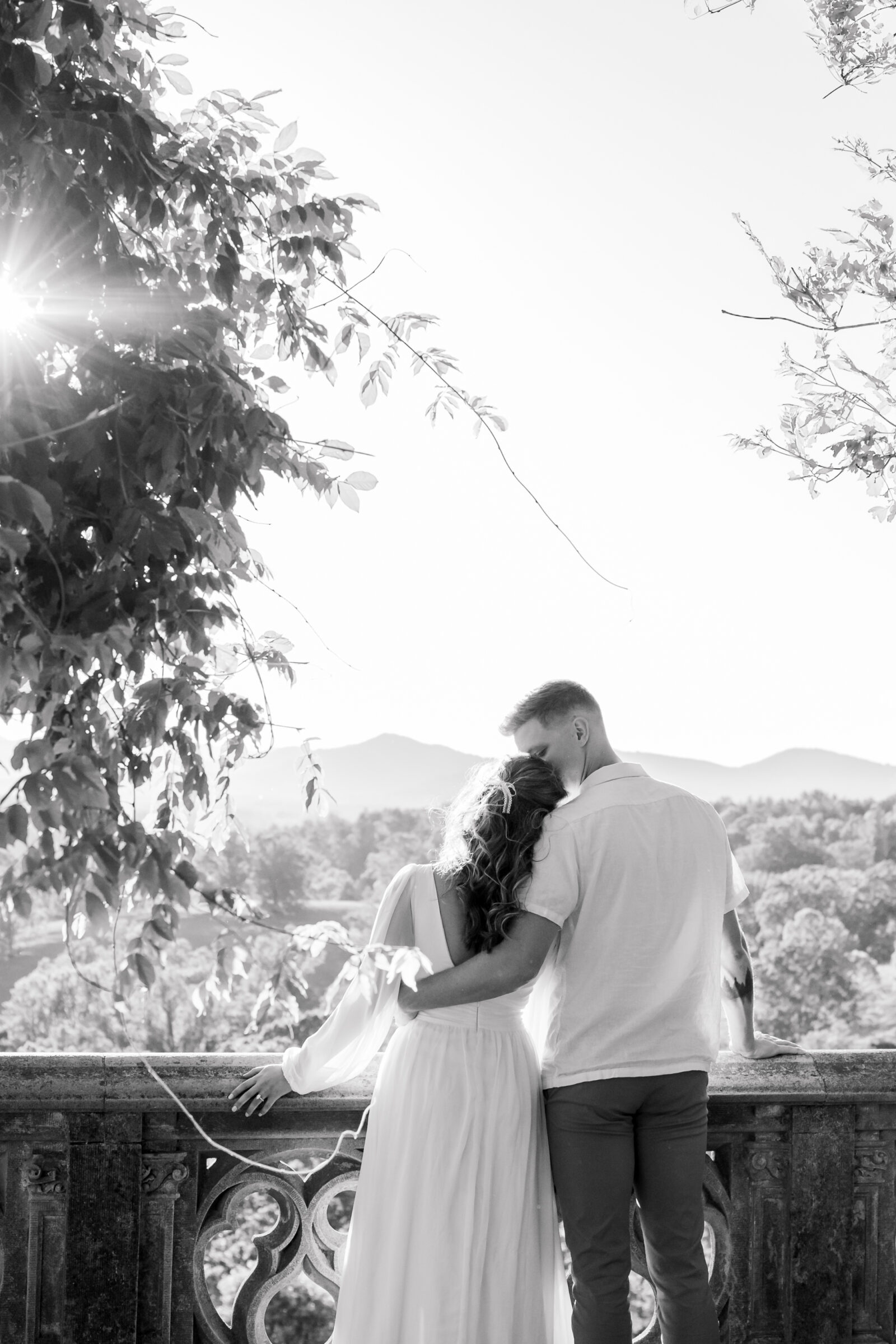 Engagement Photos at the Biltmore Estate | sun peeks into the image as a guy kisses girl's forehead on the Biltmore terrace