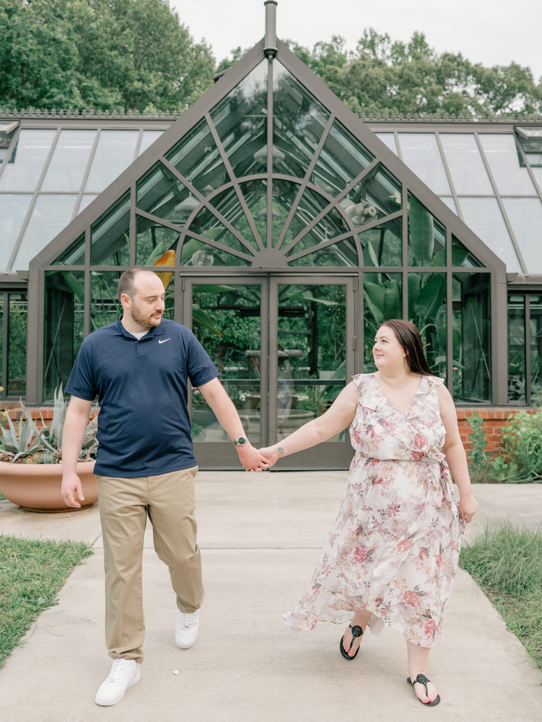 Meadowlark Botanical Gardens Engagement Session | couple walks hand in hand in front of the Meadowlark Botanical Gardens greenhouse in Northern Virginia
