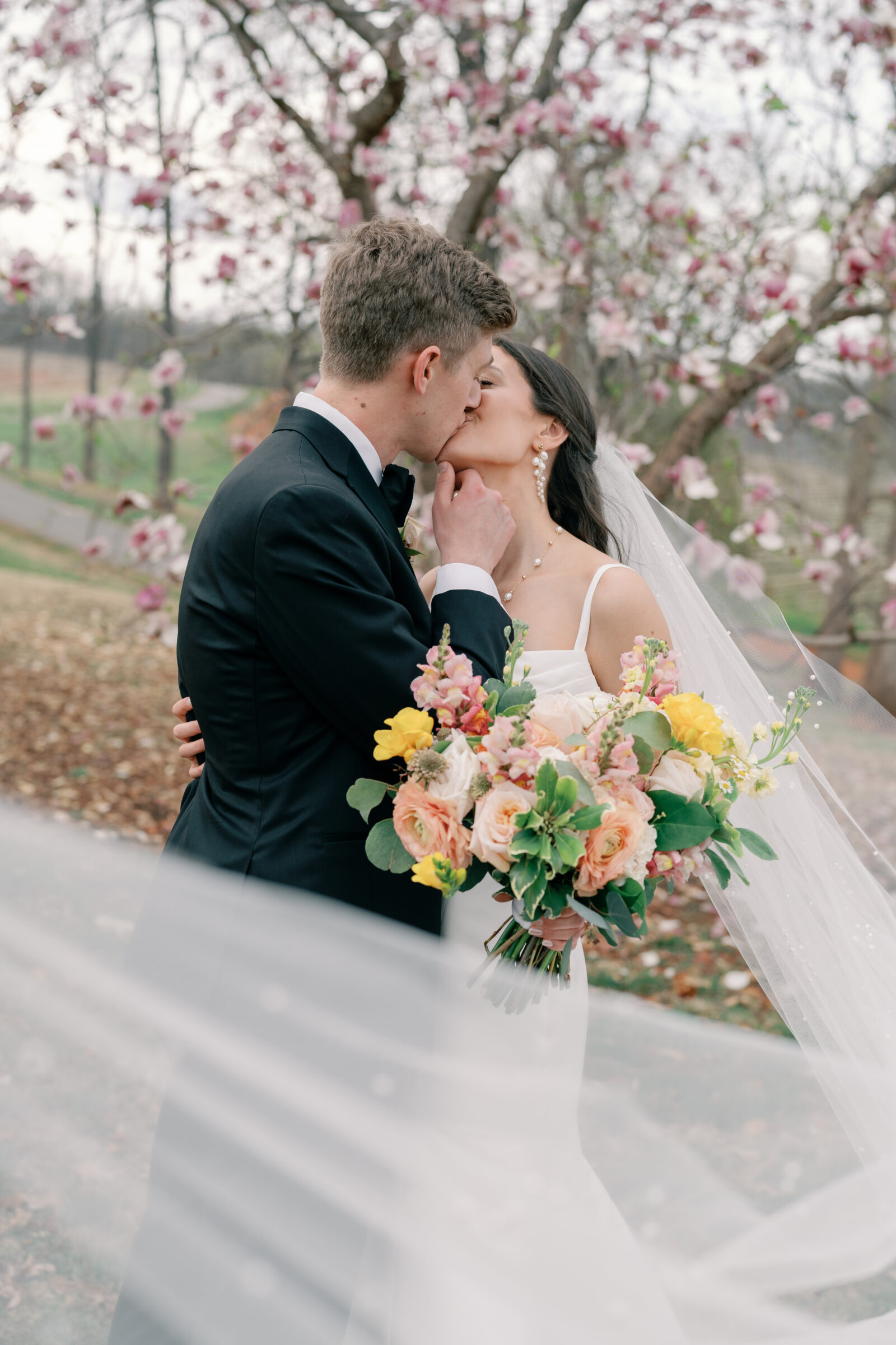 Trump Winery Grand Hall in Charlottesville, VA | bride and groom share a kiss amidst magnolia blossoms