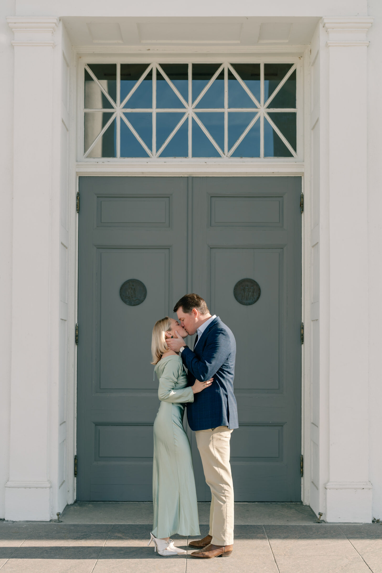 Virginia State Capitol Building Engagement Photos Richmond VA | newly engaged couple in green dress and blue suit share a kiss in front of the door to the Virginia Capitol Building