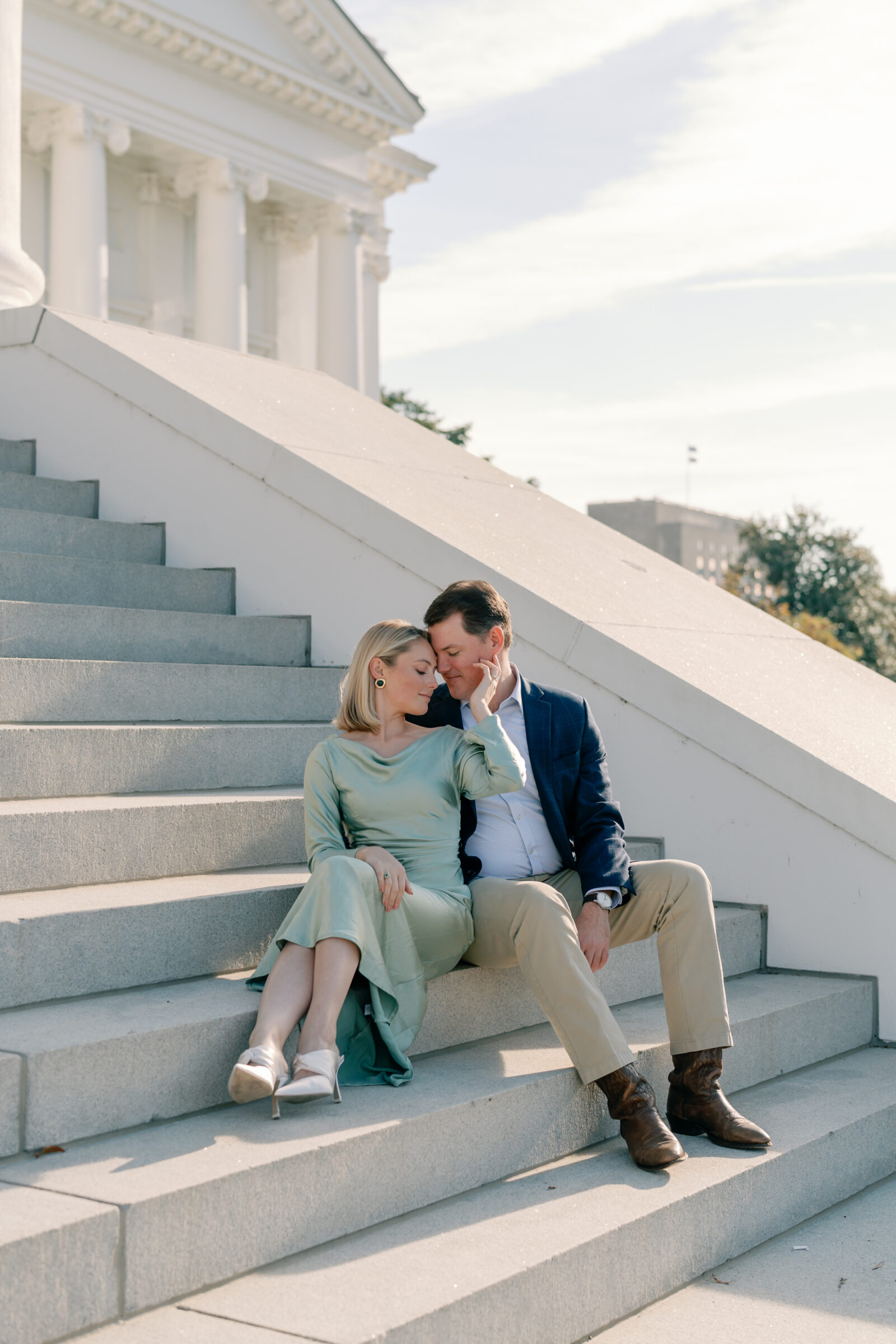 Virginia Capitol Building Engagement Session Richmond VA | couple in green dress and blue suit sit on the grand white staircase of the Virginia Capitol