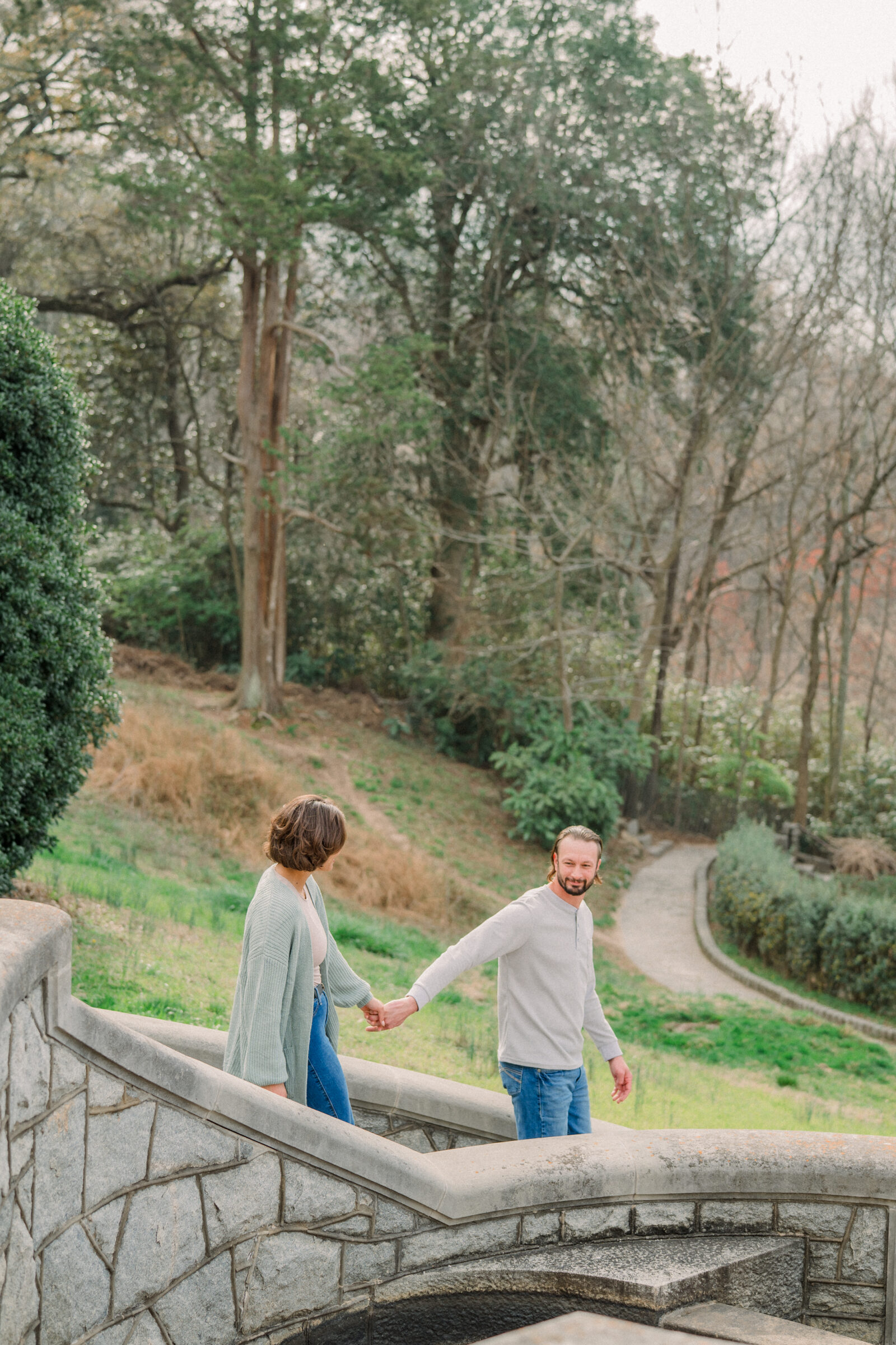 Engaged couple holding hands as they descend a weathered stone staircase surrounded by lush greenery during their Maymont Park engagement session