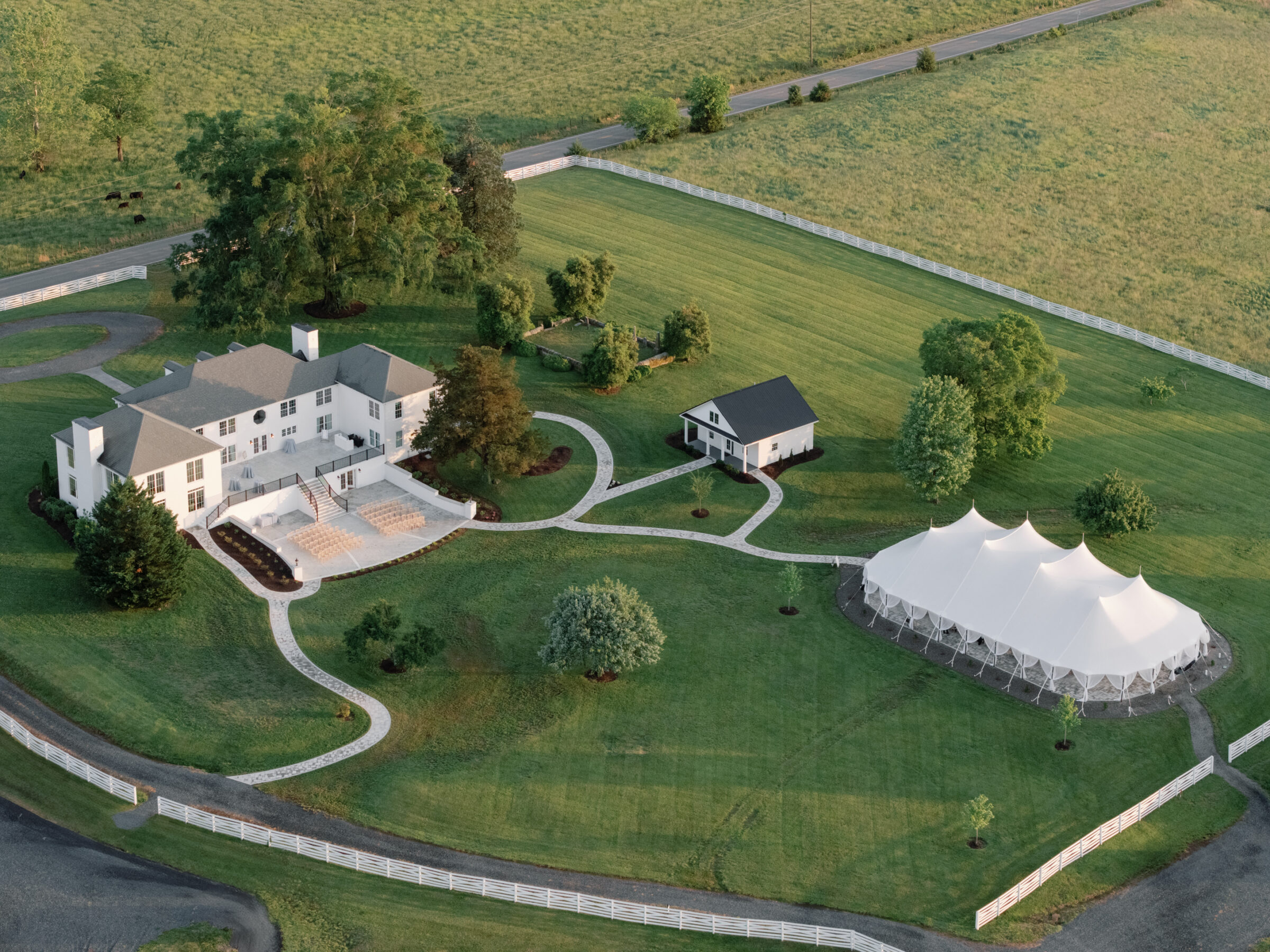 Aerial view of Northfield Estate in Cumberland, VA, featuring the elegant white manor house, a sailcloth tent for wedding receptions, manicured lawns, winding white fences, and a charming black-roofed cottage—all nestled in the Virginia countryside just outside Richmond.