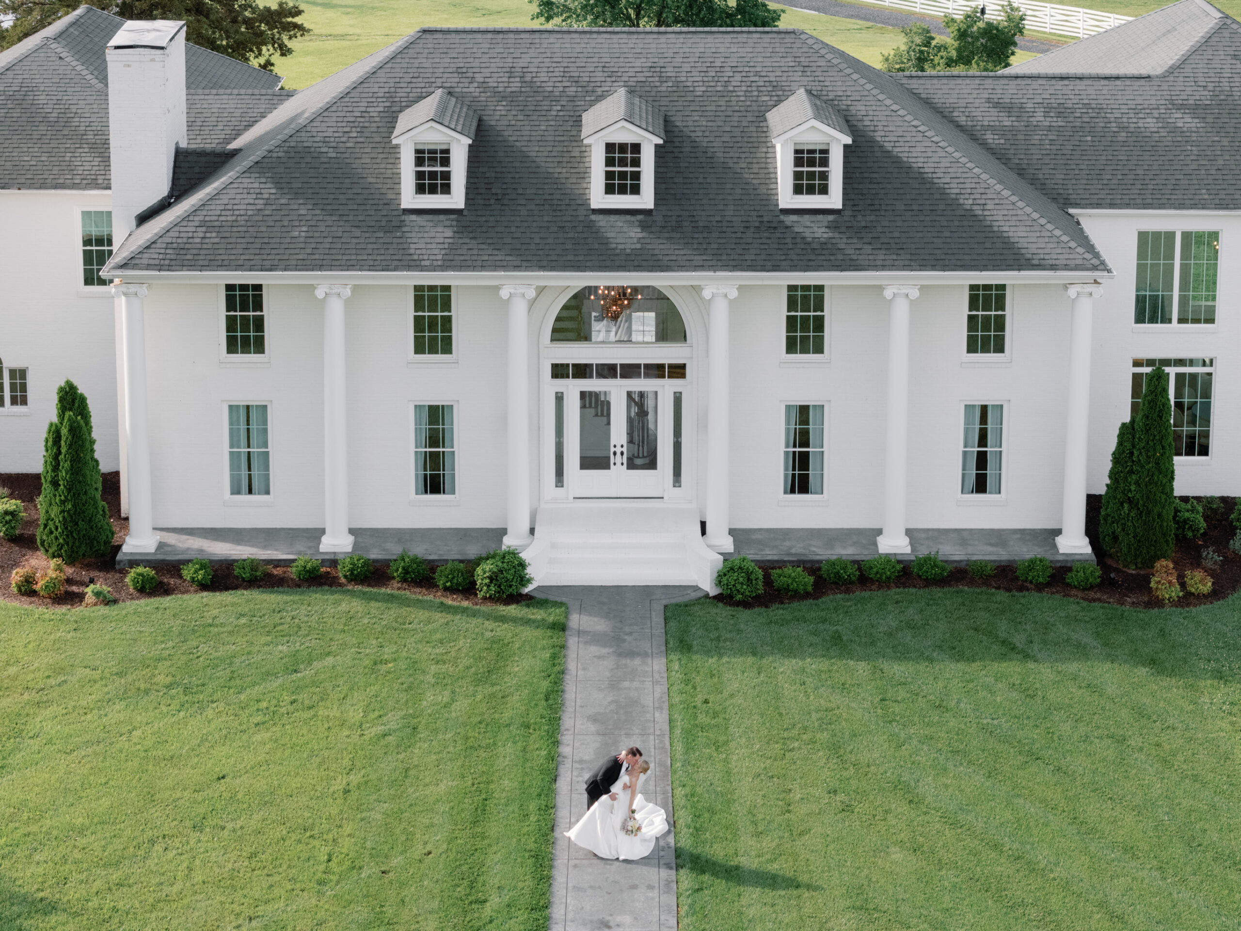 Aerial view of the bride and groom kissing in front of Northfield Estate in Cumberland, VA, with the grand white-columned mansion as a timeless and elegant backdrop—perfect for a romantic wedding day near Richmond.