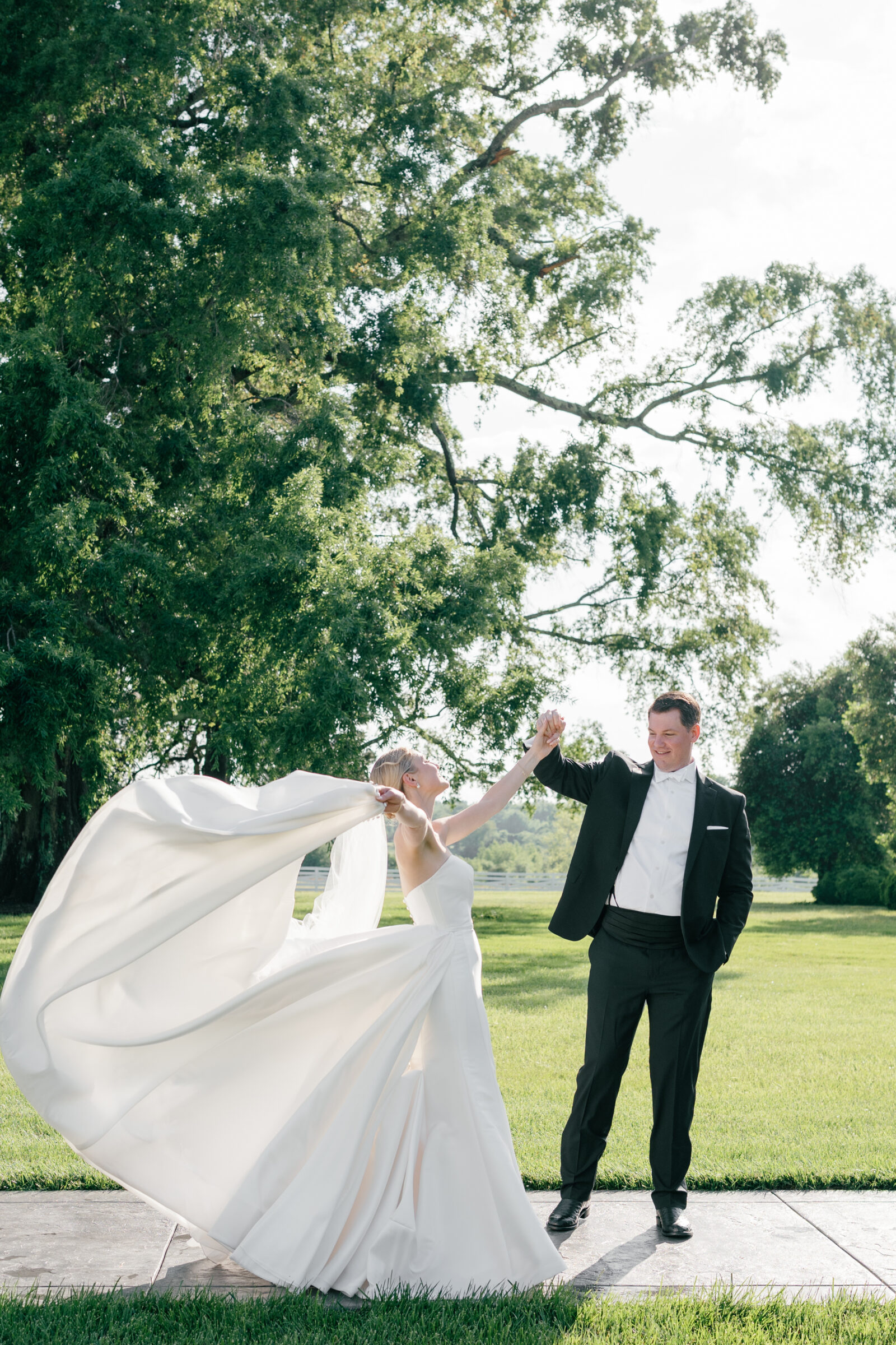 Bride twirling joyfully with her groom in the gardens of Northfield Estate in Cumberland, VA, her satin gown flowing dramatically in the breeze—capturing a playful and romantic wedding day moment near Richmond.