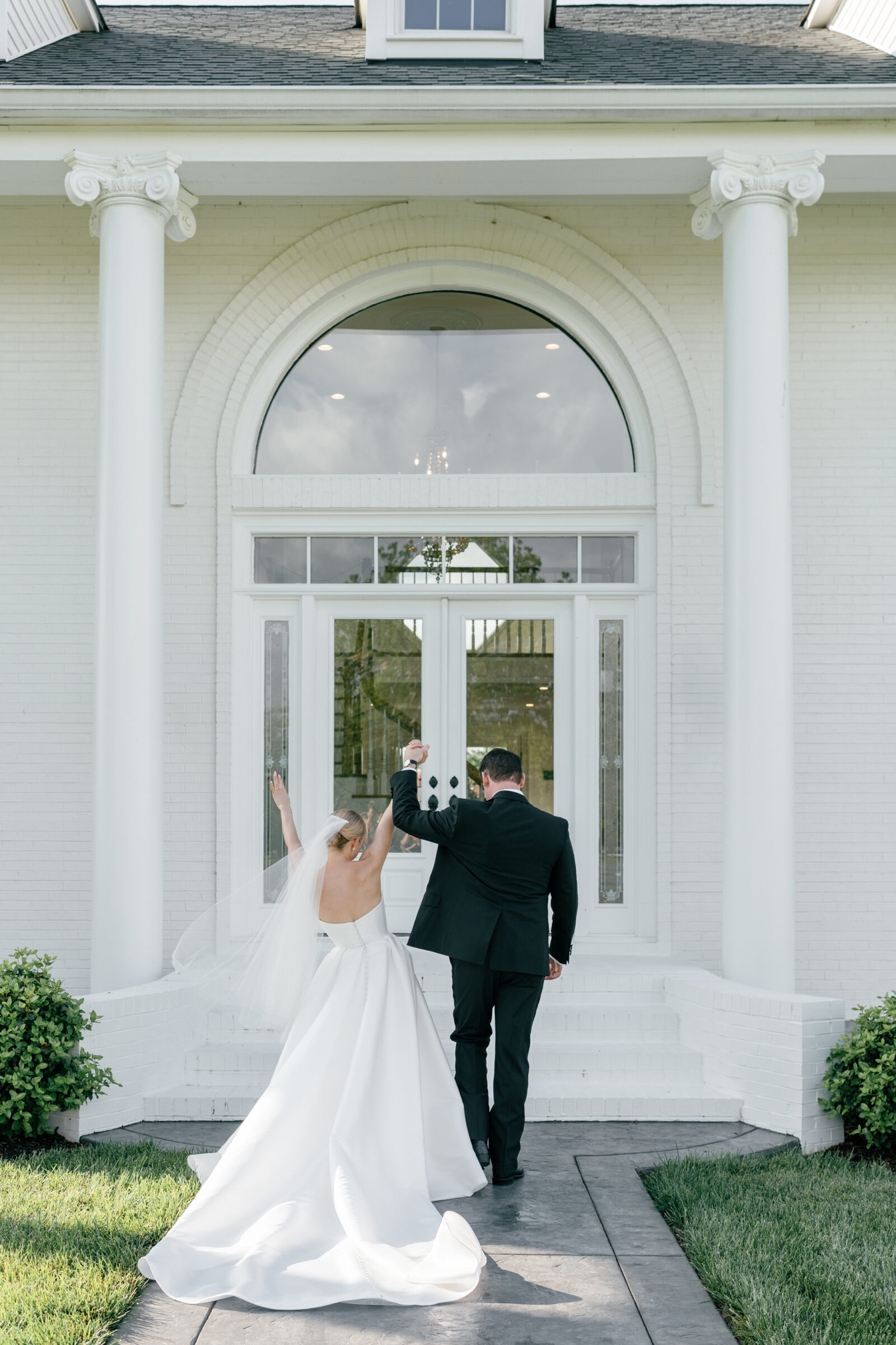 Bride and groom celebrating outside the grand entrance of Northfield Estate in Cumberland, VA, holding hands beneath white columns and arched windows—capturing the timeless charm of this Virginia wedding venue near Richmond.