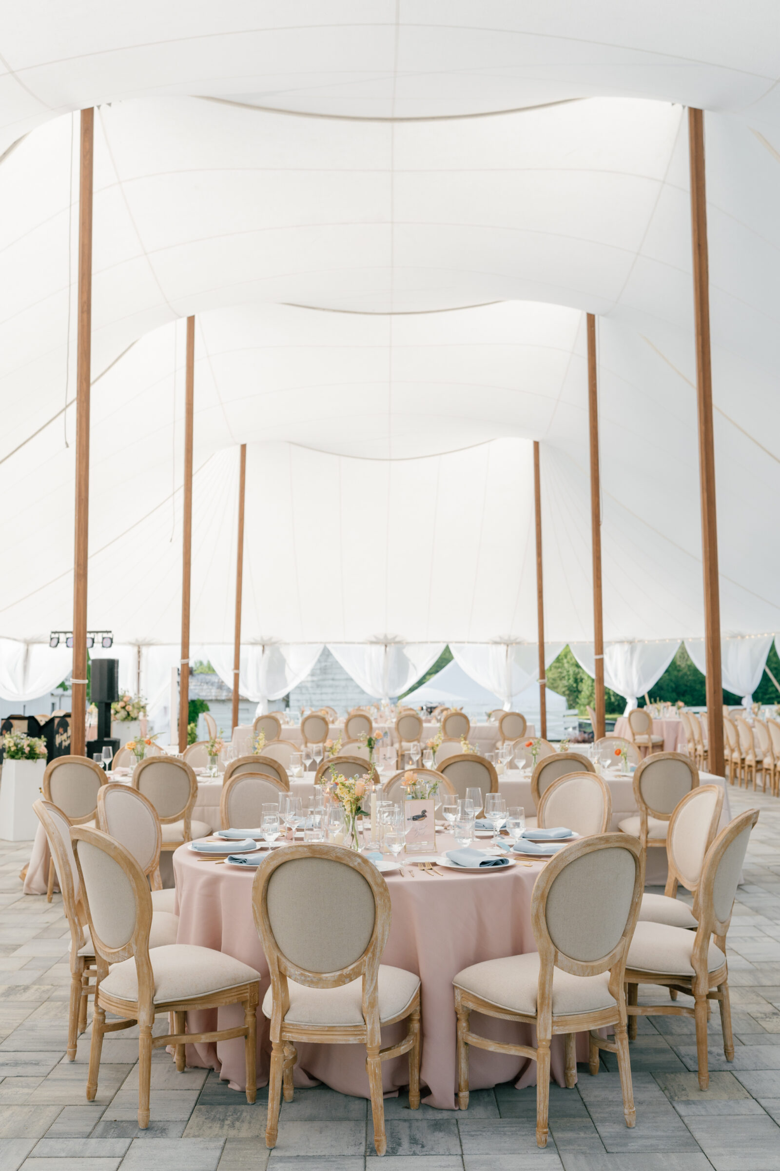 Tented wedding reception at Northfield Estate in Cumberland, VA, with round tables dressed in blush linens, natural upholstered chairs, and soft floral centerpieces beneath an elegant sailcloth tent—perfect for a refined Virginia wedding near Richmond.