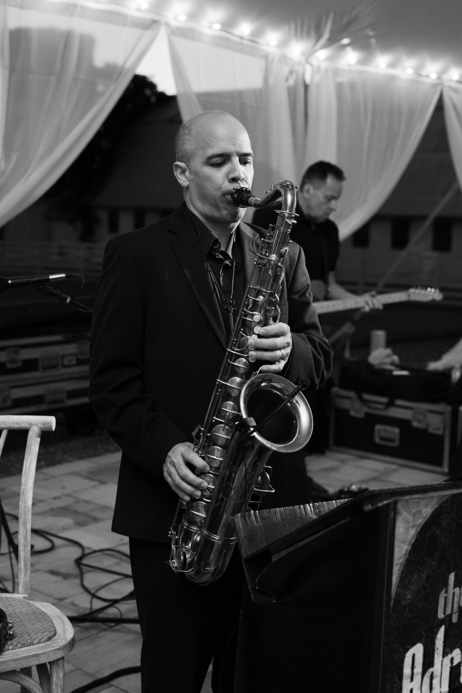A black-and-white photo of a saxophonist performing live during a spring Northfield Estate wedding reception in Cumberland, VA, captured by a Richmond wedding photographer beneath a sailcloth tent with romantic draping and string lights.