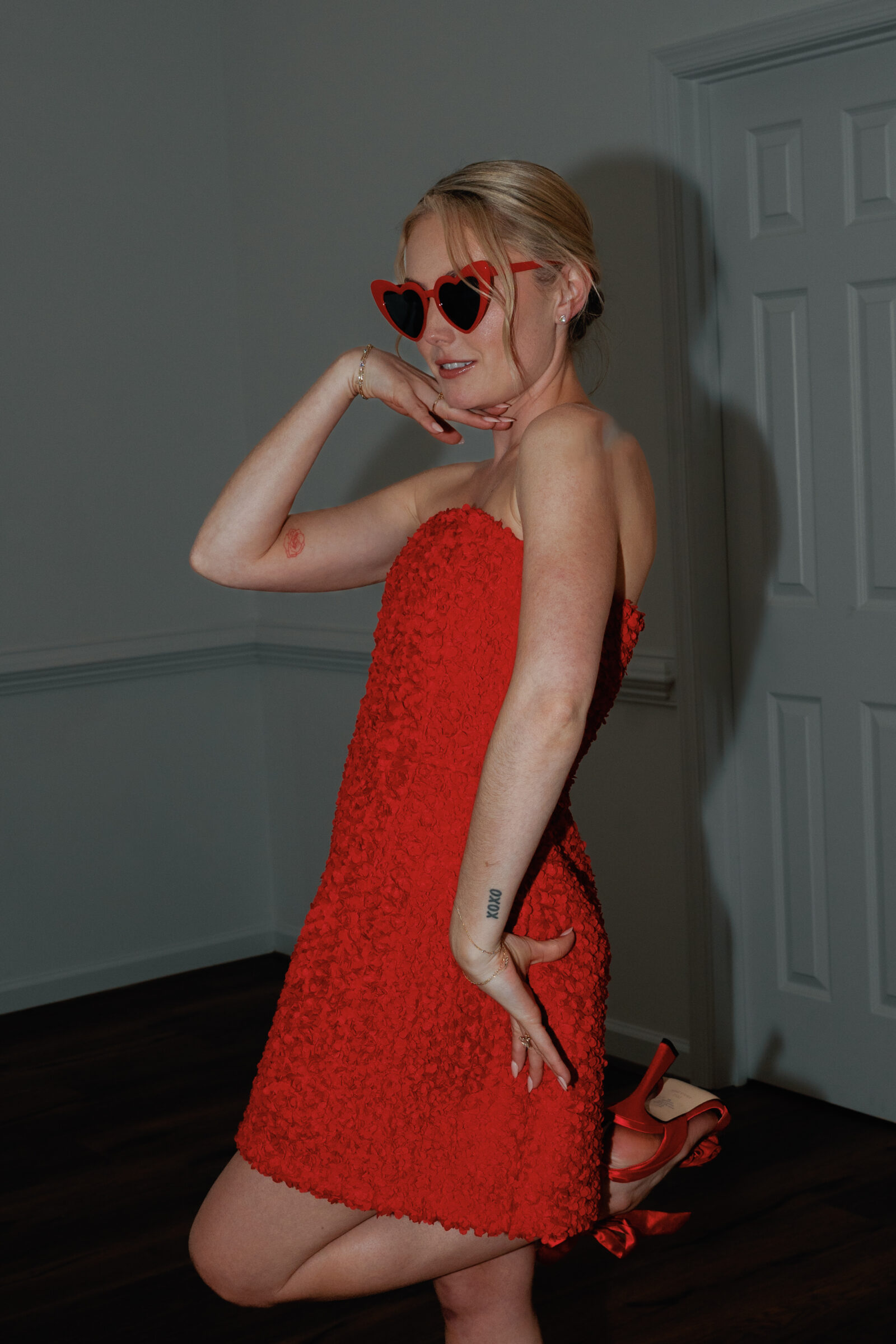 Bride poses playfully in a red textured mini dress with heart-shaped sunglasses and matching red heels during a spring Northfield Estate wedding in Cumberland, VA, photographed with editorial flash by a Richmond wedding photographer.