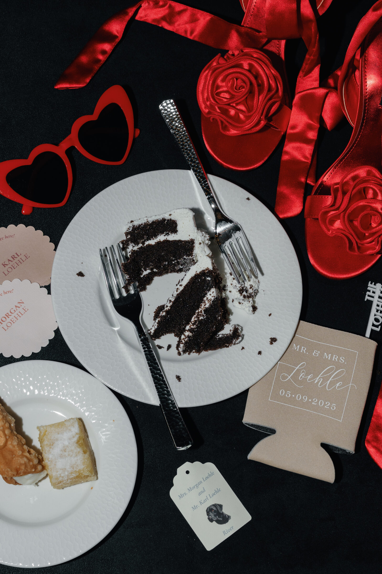 Flat lay of chocolate wedding cake, custom koozie, red heart sunglasses, and red rosette heels captured during a spring Northfield Estate wedding in Cumberland, VA, highlighting playful and personal reception details photographed by a Richmond wedding photographer.