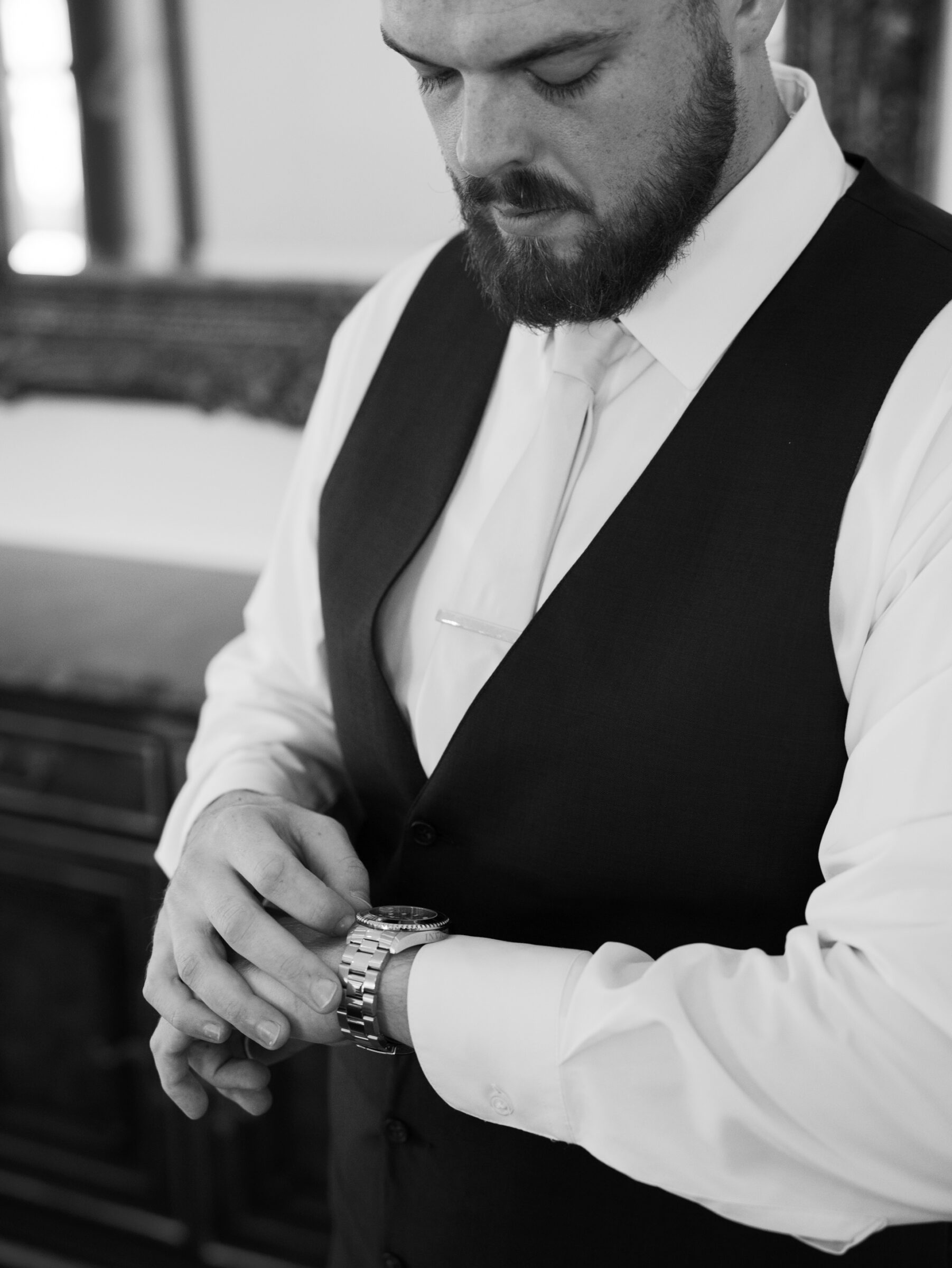 Black-and-white close‑up of groom in tailored vest adjusting his silver watch during Trump Winery Wedding preparations in Charlottesville