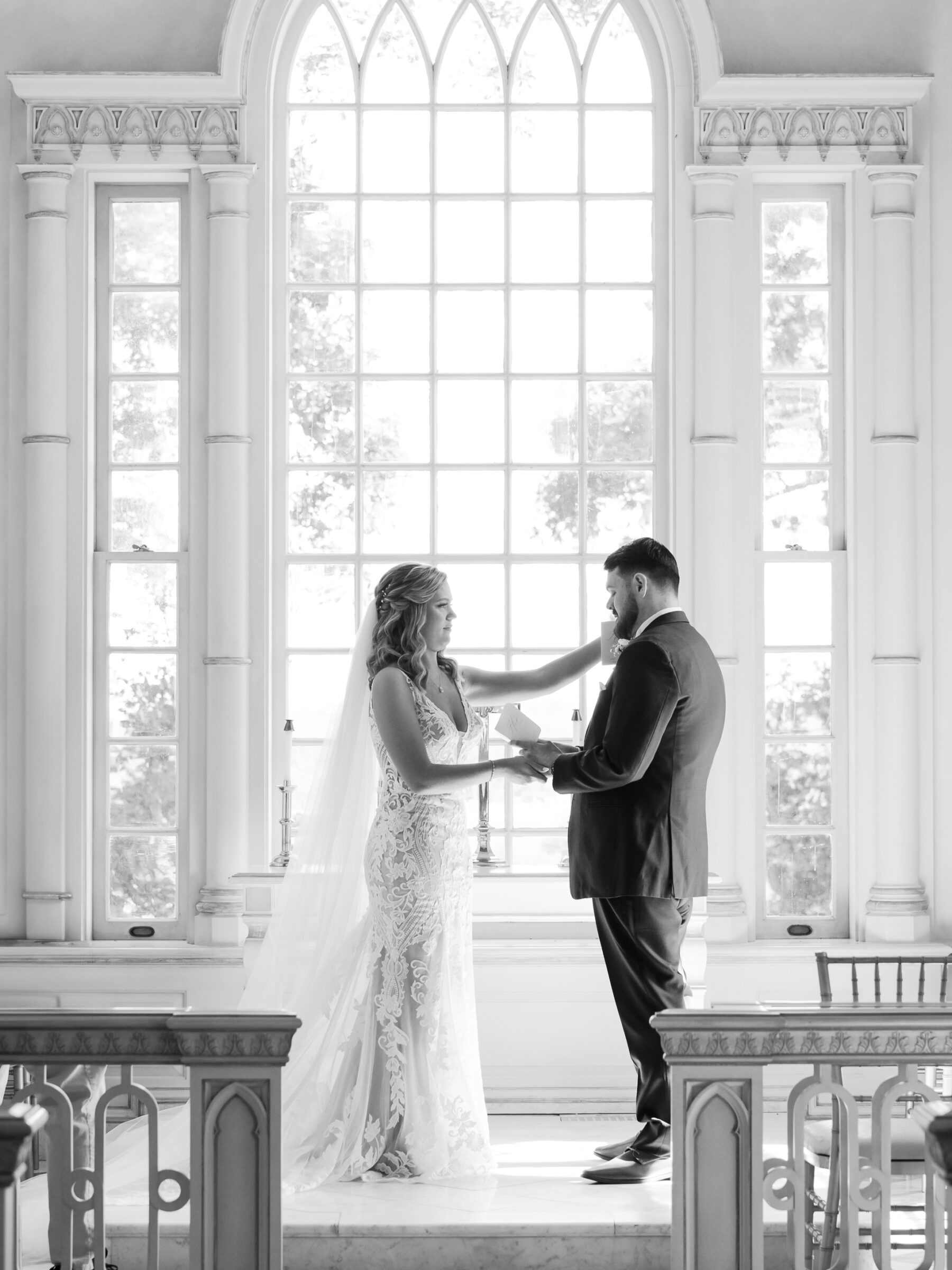Black‑and‑white silhouette of bride and groom exchanging vows before a towering arched window at their Trump Winery Wedding in Charlottesville