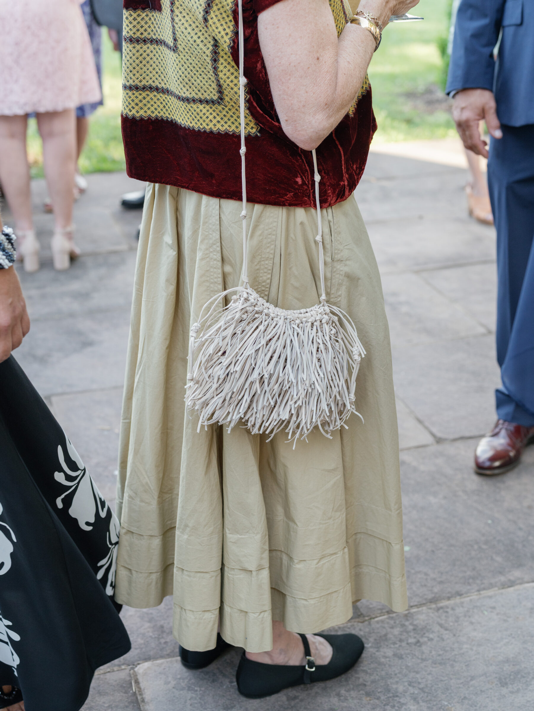 Close‑up of a cream fringe crossbody handbag worn by a wedding guest in a beige skirt and red top at a Trump Winery Wedding in Charlottesville