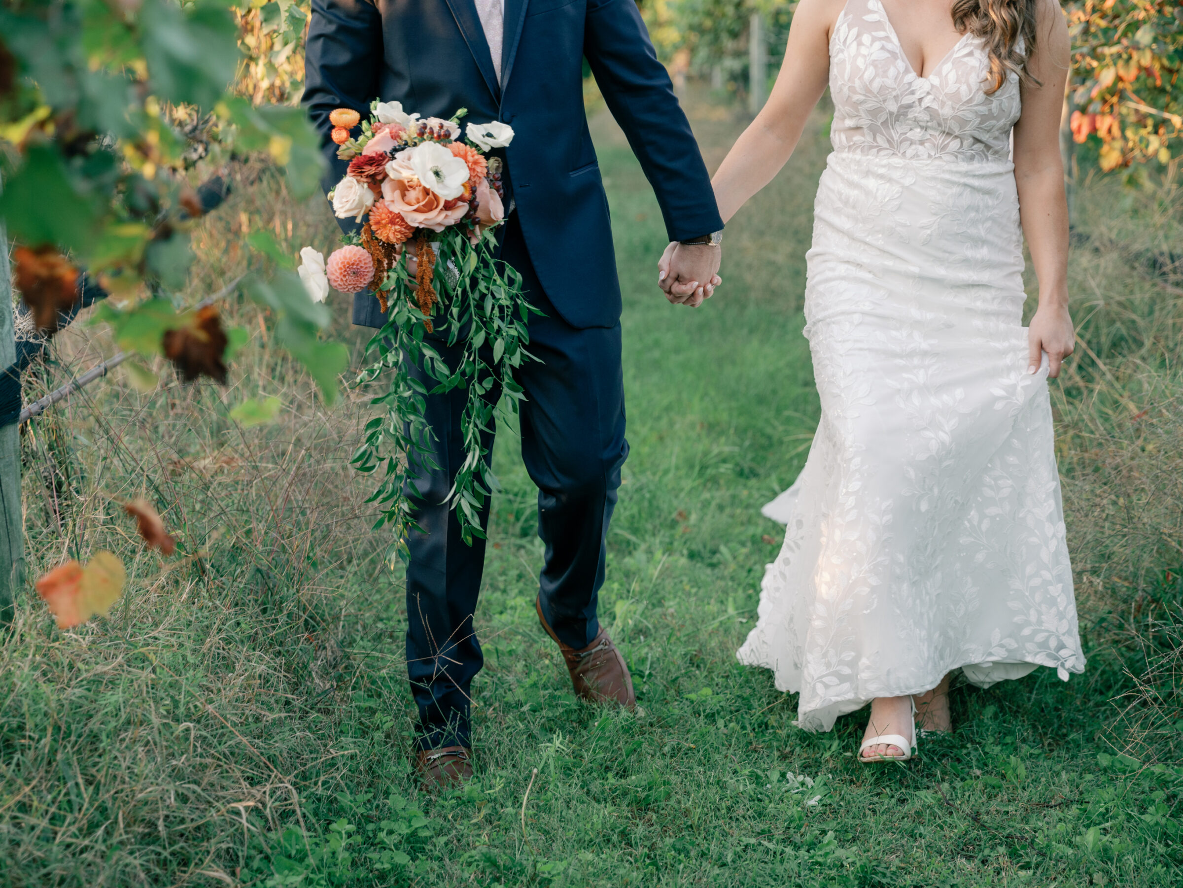 Detail photo of bride and groom holding hands while walking through vineyard rows at a vineyard wedding in Chester VA.