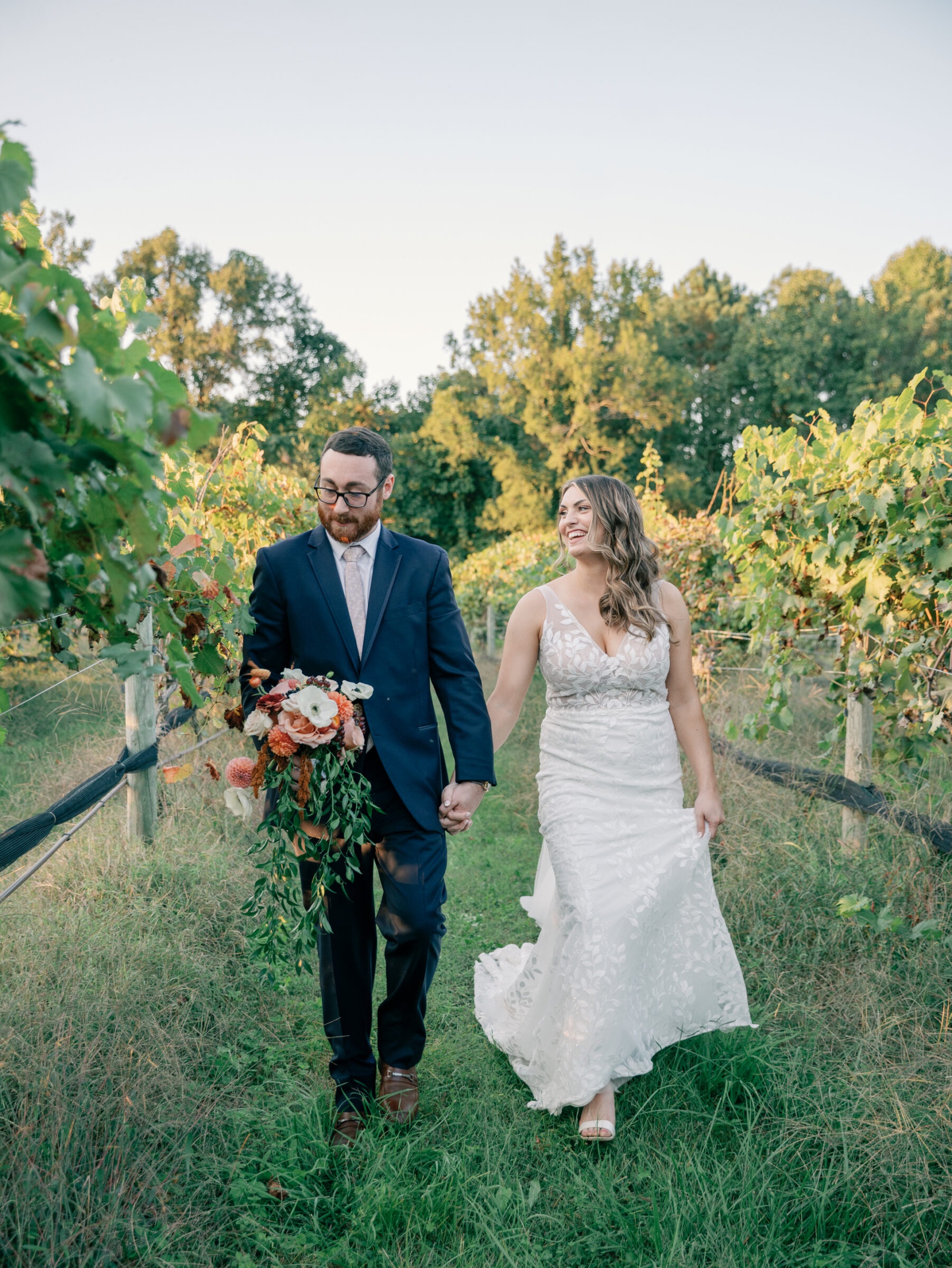 Bride and groom walking hand in hand through vineyard rows at Ashton Creek Vineyards wedding in Chester VA.