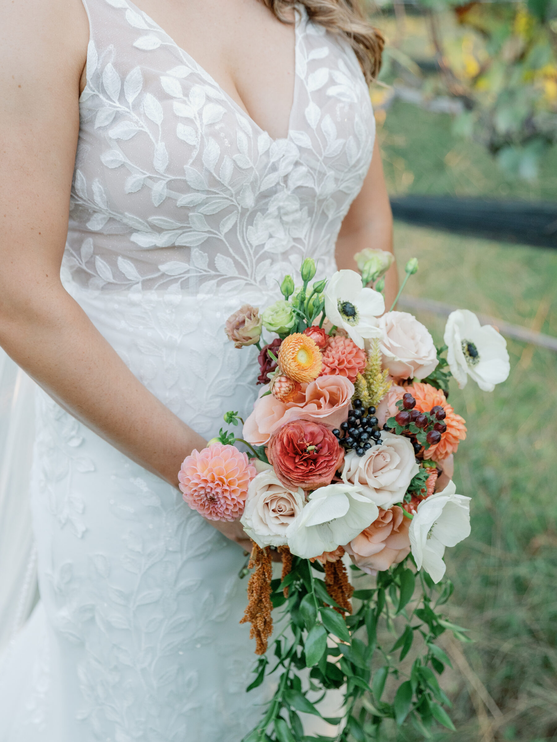 Bride holding a cascading bouquet of roses, dahlias, and anemones in soft blush and berry tones at a vineyard wedding in Chester VA.