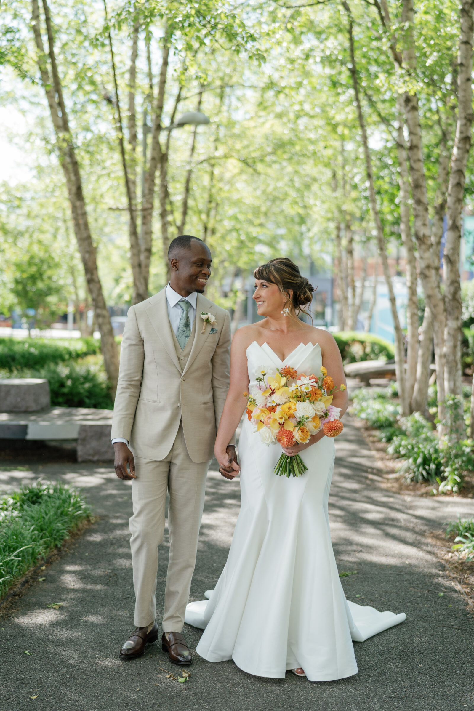 Bride and groom walking hand in hand along a tree-lined path near District Winery in Washington DC during their spring wedding portraits.