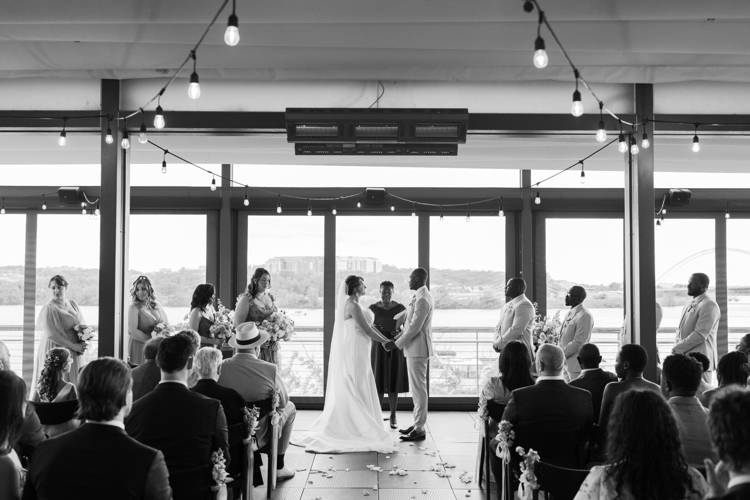 Black and white photo of a District Winery wedding ceremony in Washington DC with the couple exchanging vows indoors overlooking the Anacostia River.