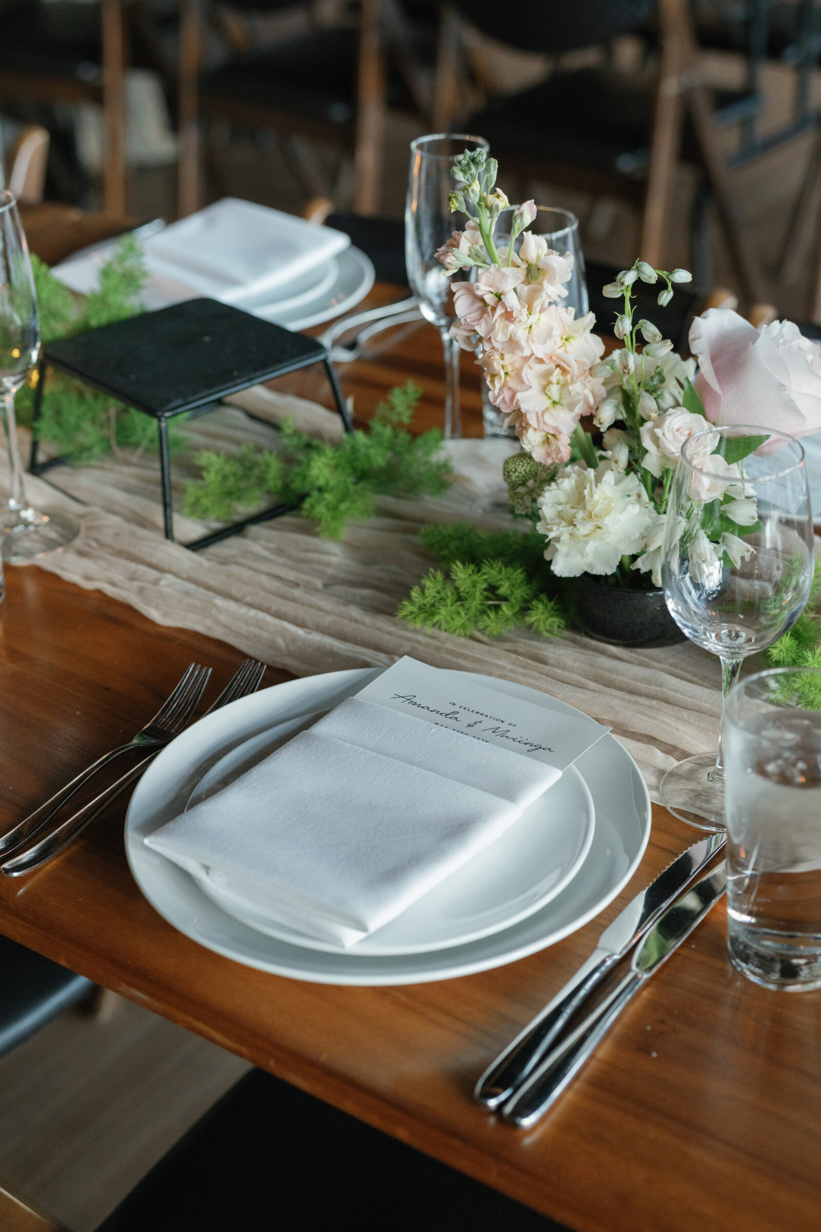 Elegant wedding table setting at District Winery in Washington DC with personalized menus, soft pastel florals, and greenery accents on wooden tables.