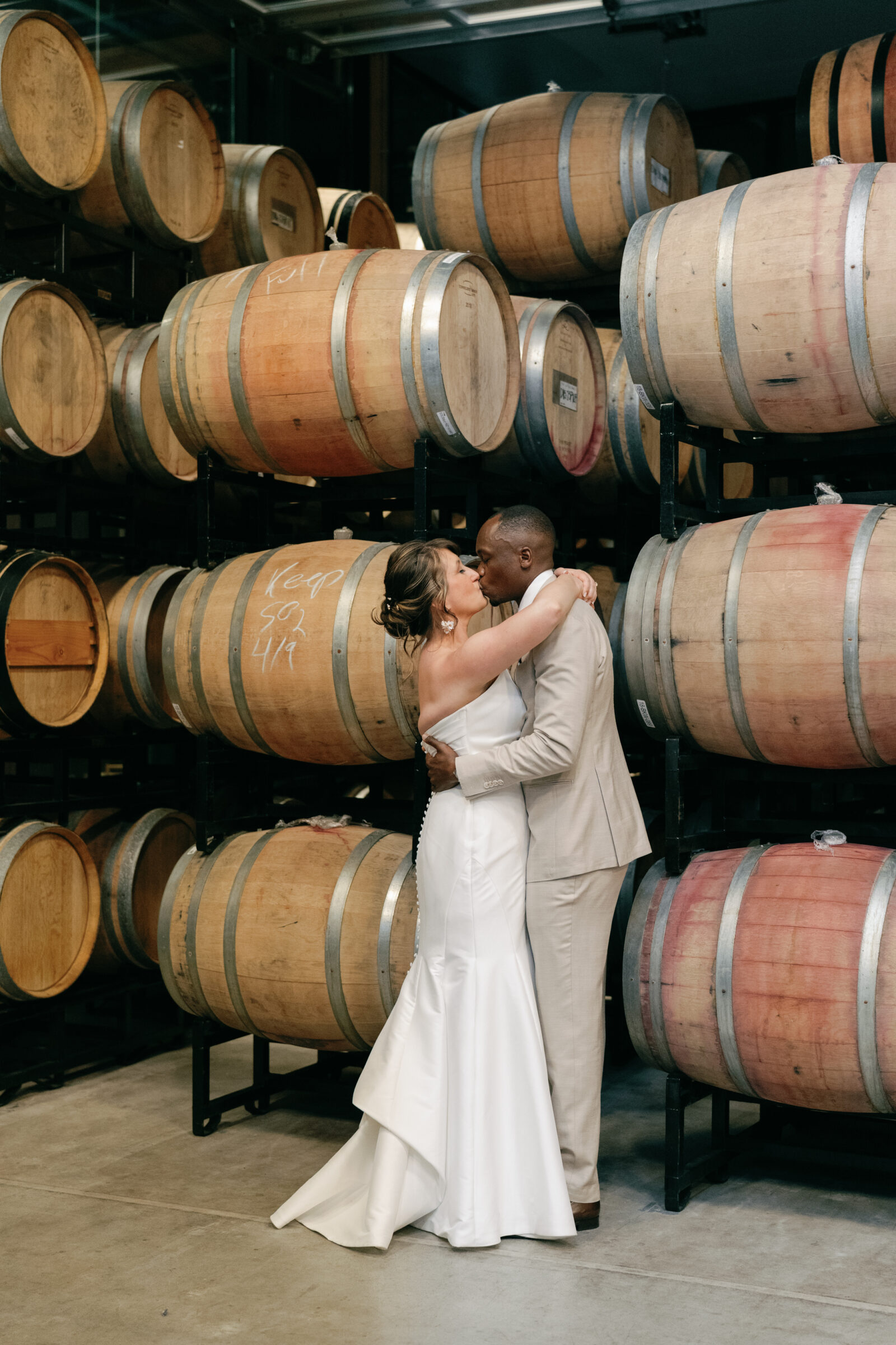 Bride and groom kissing in the wine barrel room at District Winery in Washington DC, showcasing the unique indoor spaces for wedding portraits.