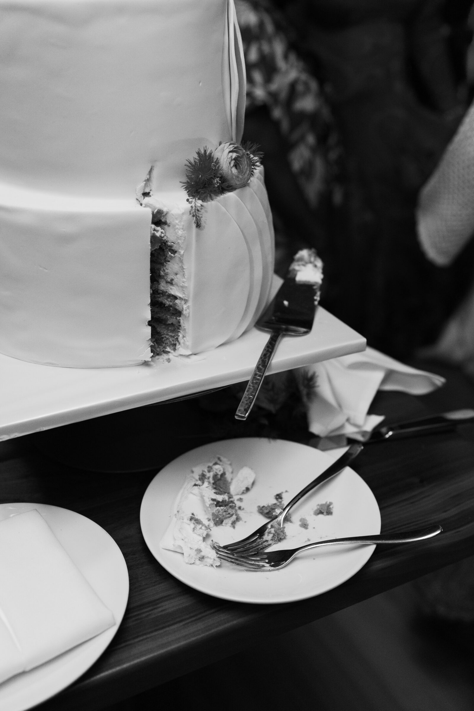 Black and white photo of a wedding cake at District Winery in Washington DC with a slice cut and served on a plate during the reception.