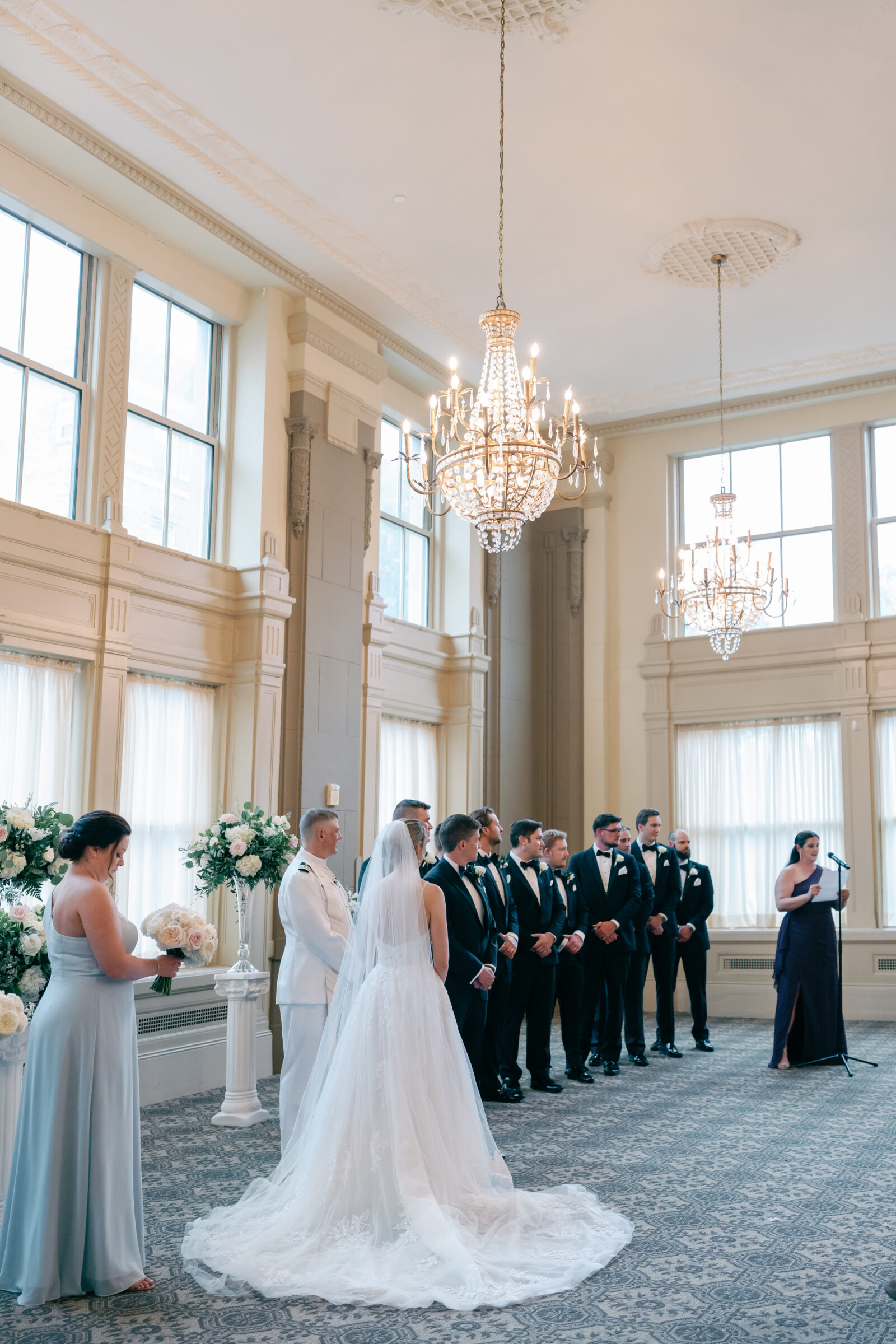 Wedding ceremony in the Virginia Ballroom at the Hotel John Marshall in Richmond VA with elegant chandeliers and tall windows.
