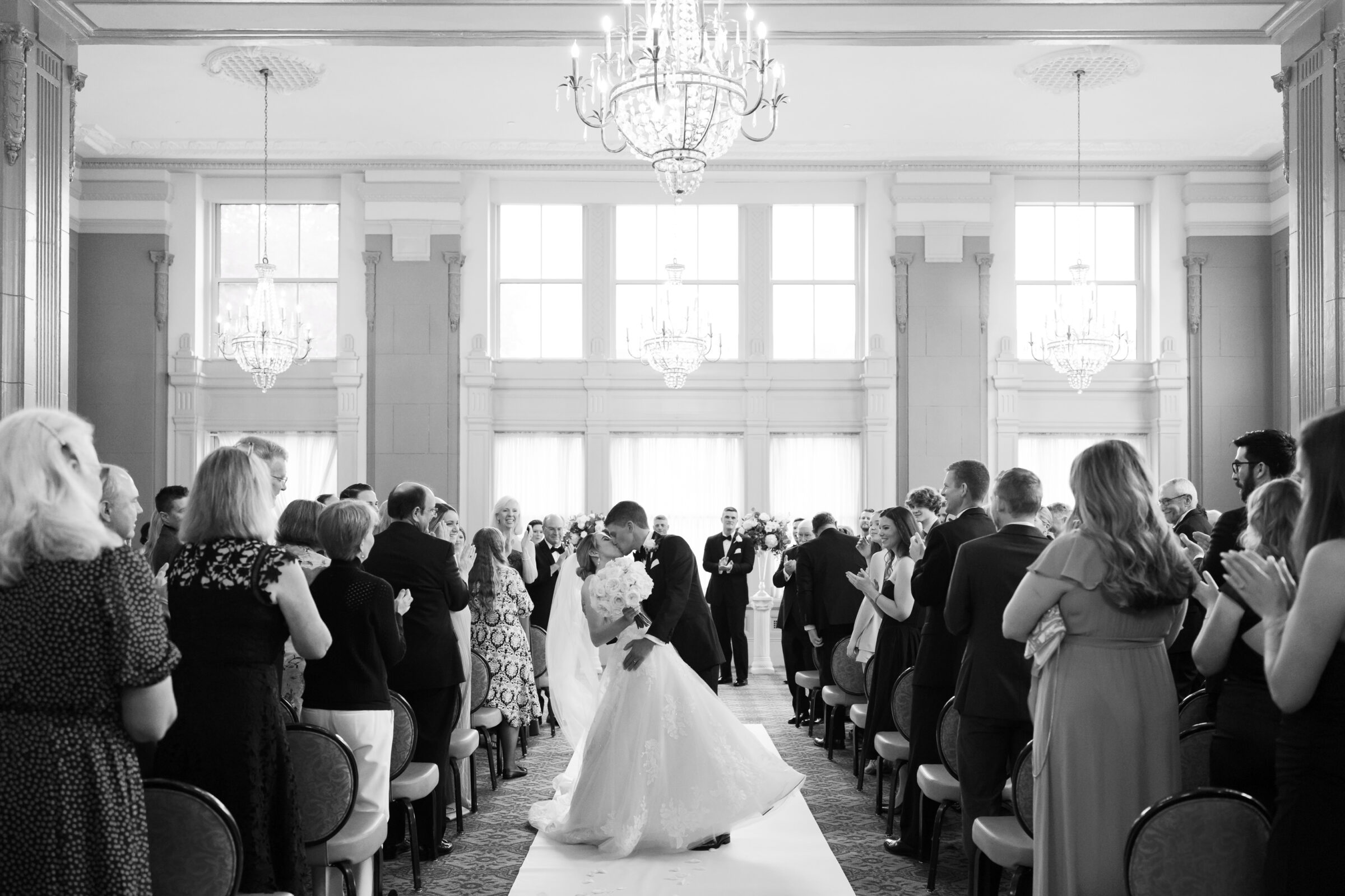 Bride and groom sharing a kiss at the end of the aisle as guests applaud during their Virginia Ballroom wedding at the Hotel John Marshall in Richmond VA.