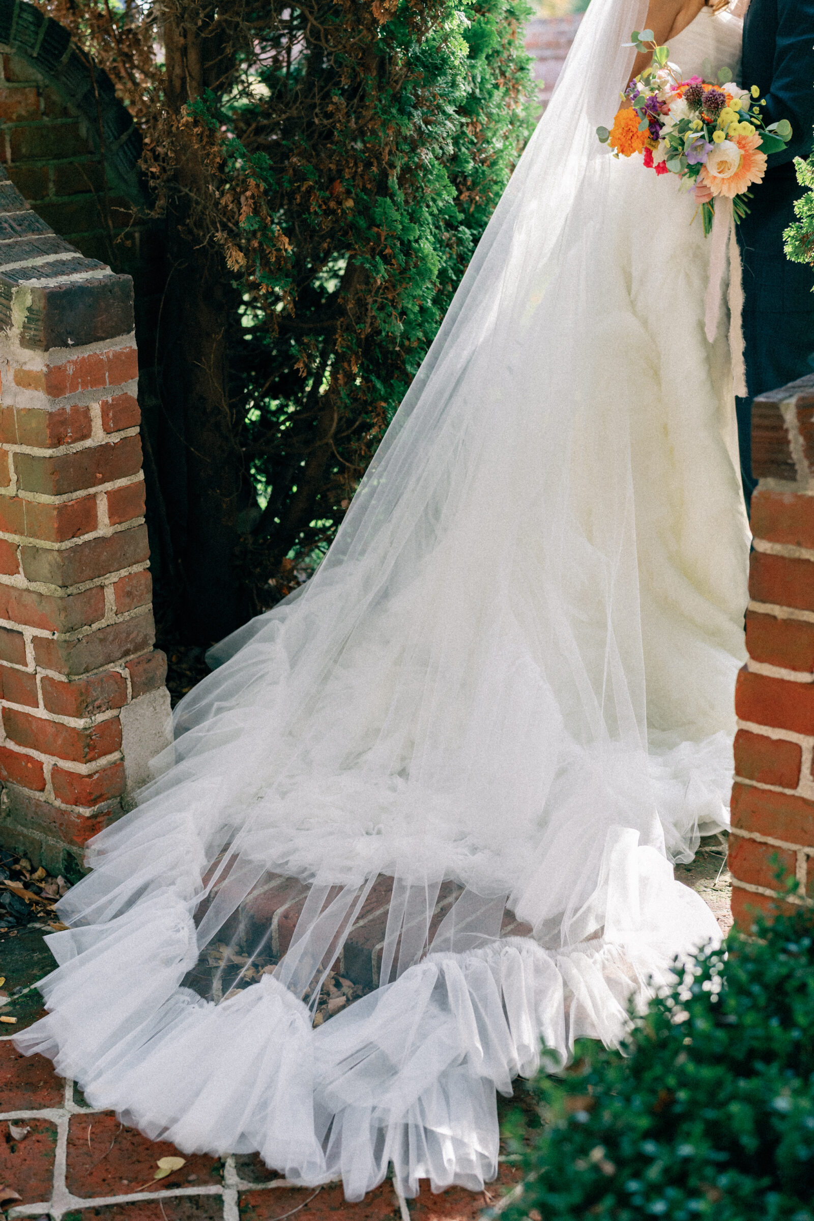 Bride and groom at Mankin Mansion in Richmond VA with a flowing cathedral veil and colorful bouquet, captured against historic brick garden walls.