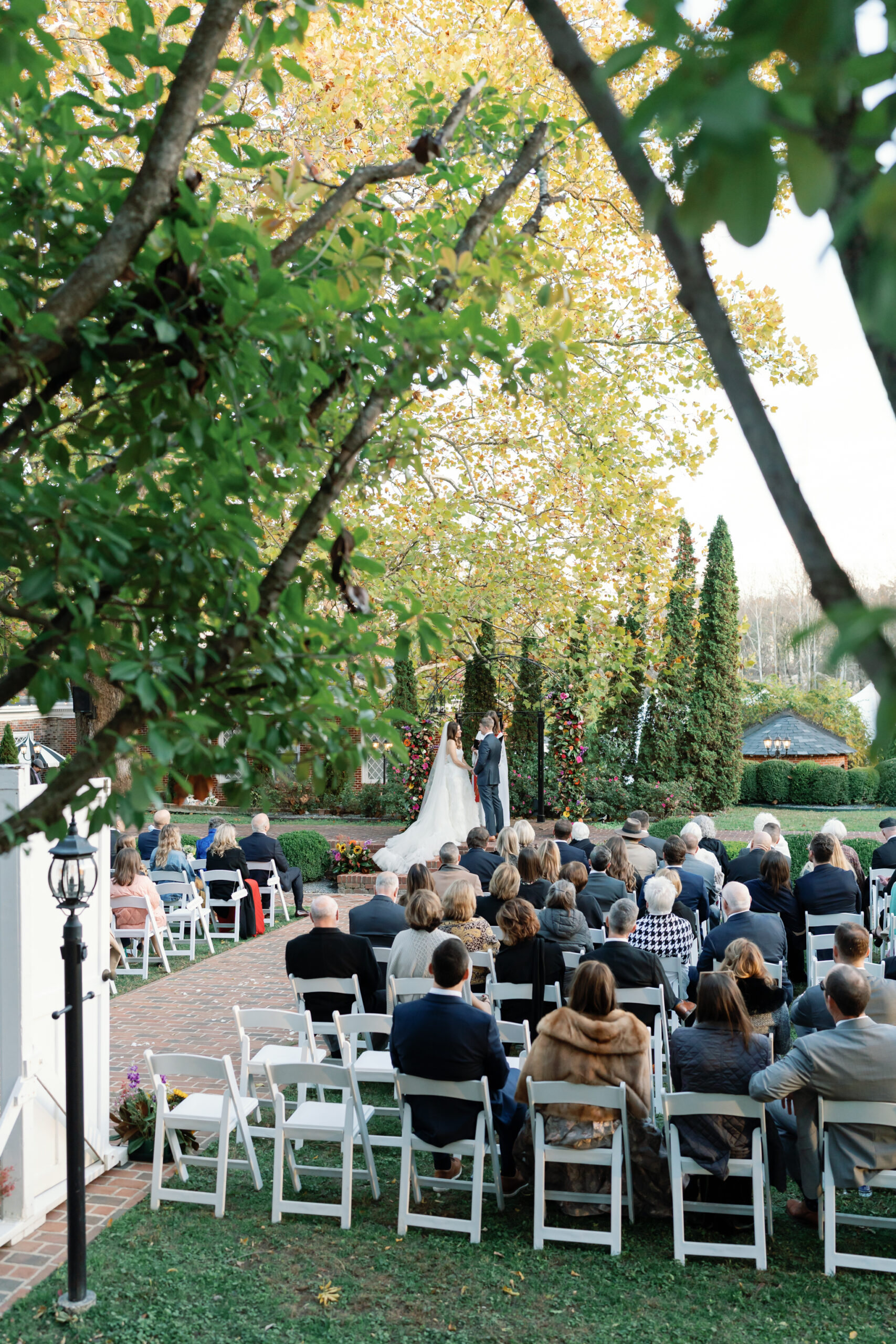 Outdoor garden ceremony at Mankin Mansion in Richmond VA with the bride and groom exchanging vows under a floral arch surrounded by family and friends.