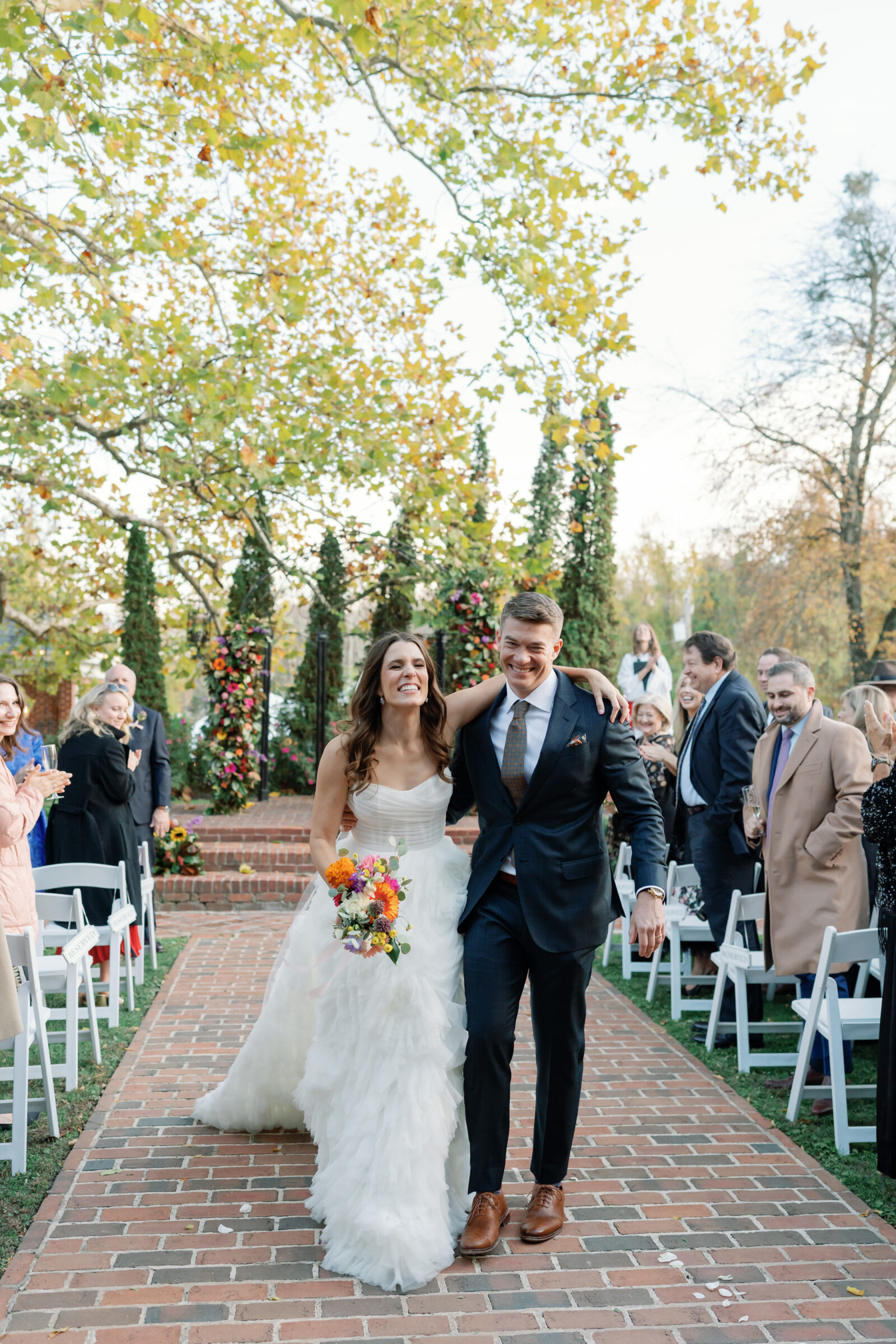 Just married couple celebrating their Mankin Mansion wedding in Richmond VA, walking down the brick aisle with colorful bouquet and smiling guests.